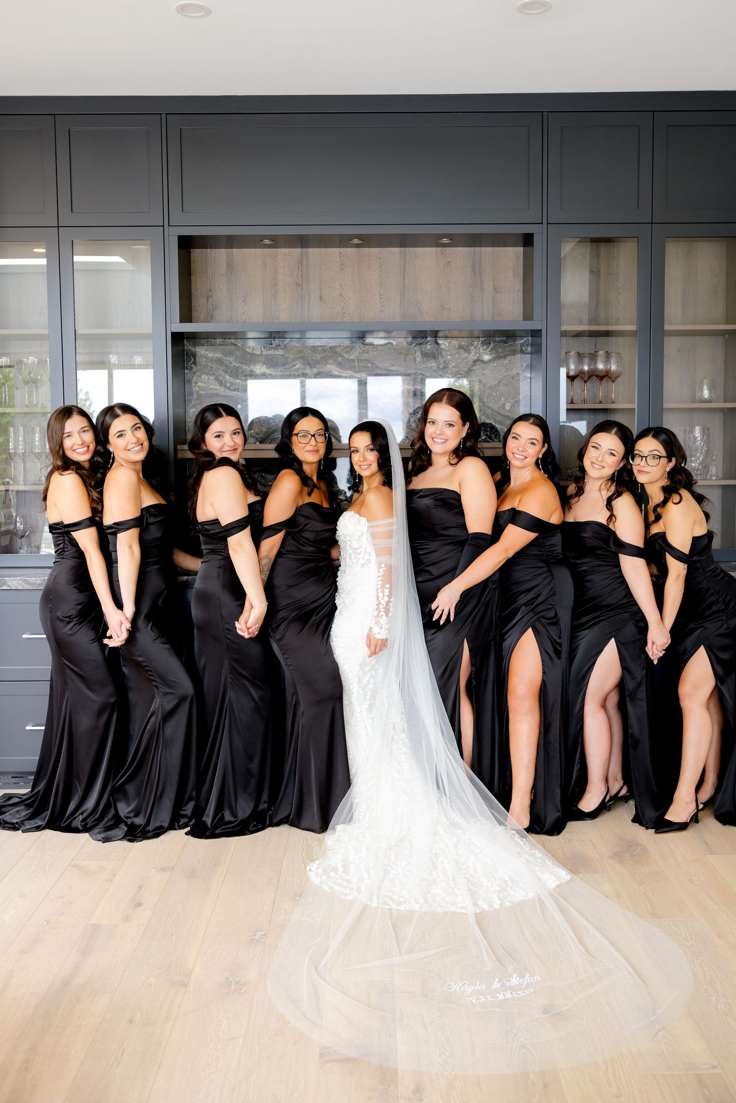 Joyful bridal party poses together showing off black bridesmaid dresses with side slits.
