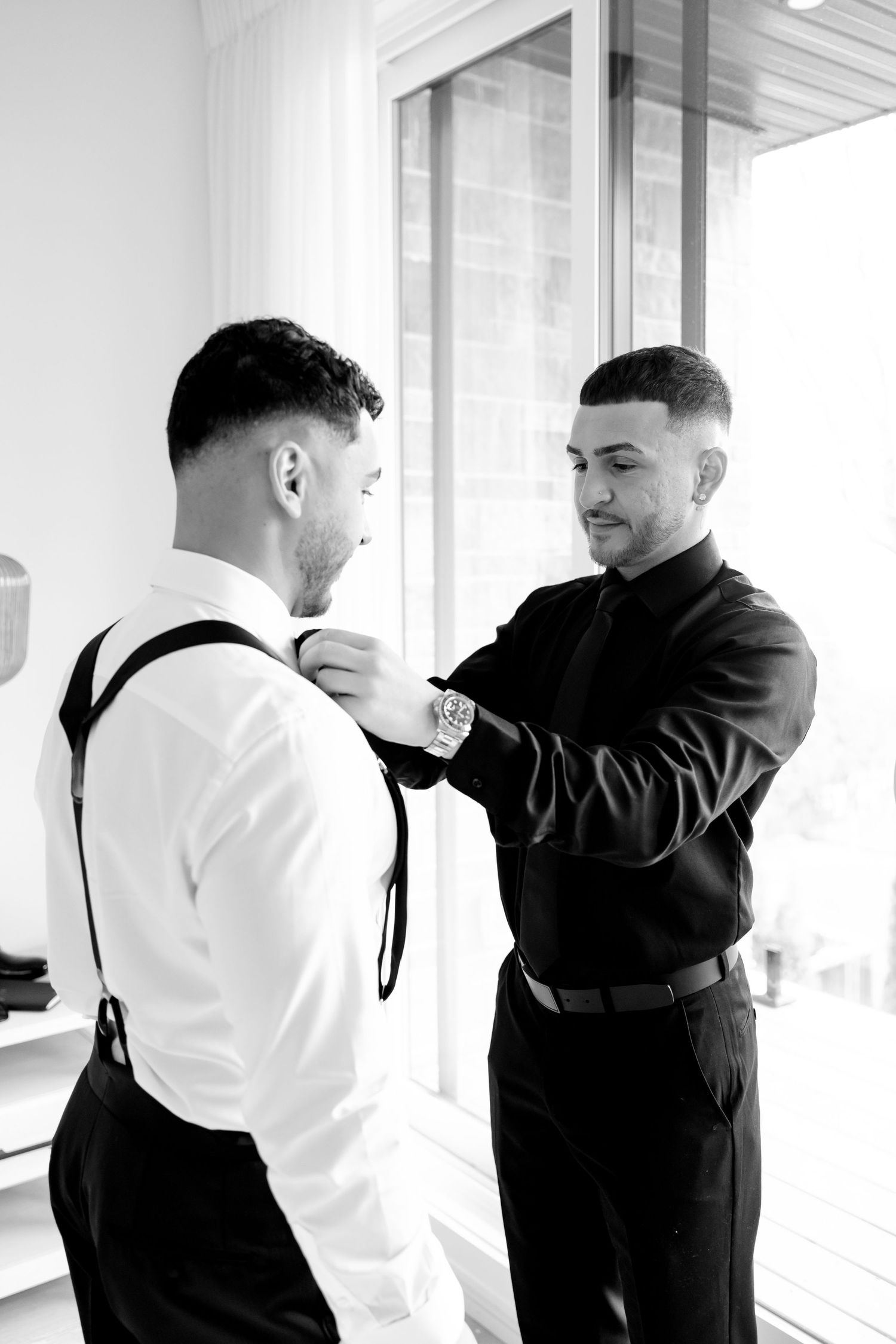 Wedding preparation showing adjustments to formal attire near bright window.