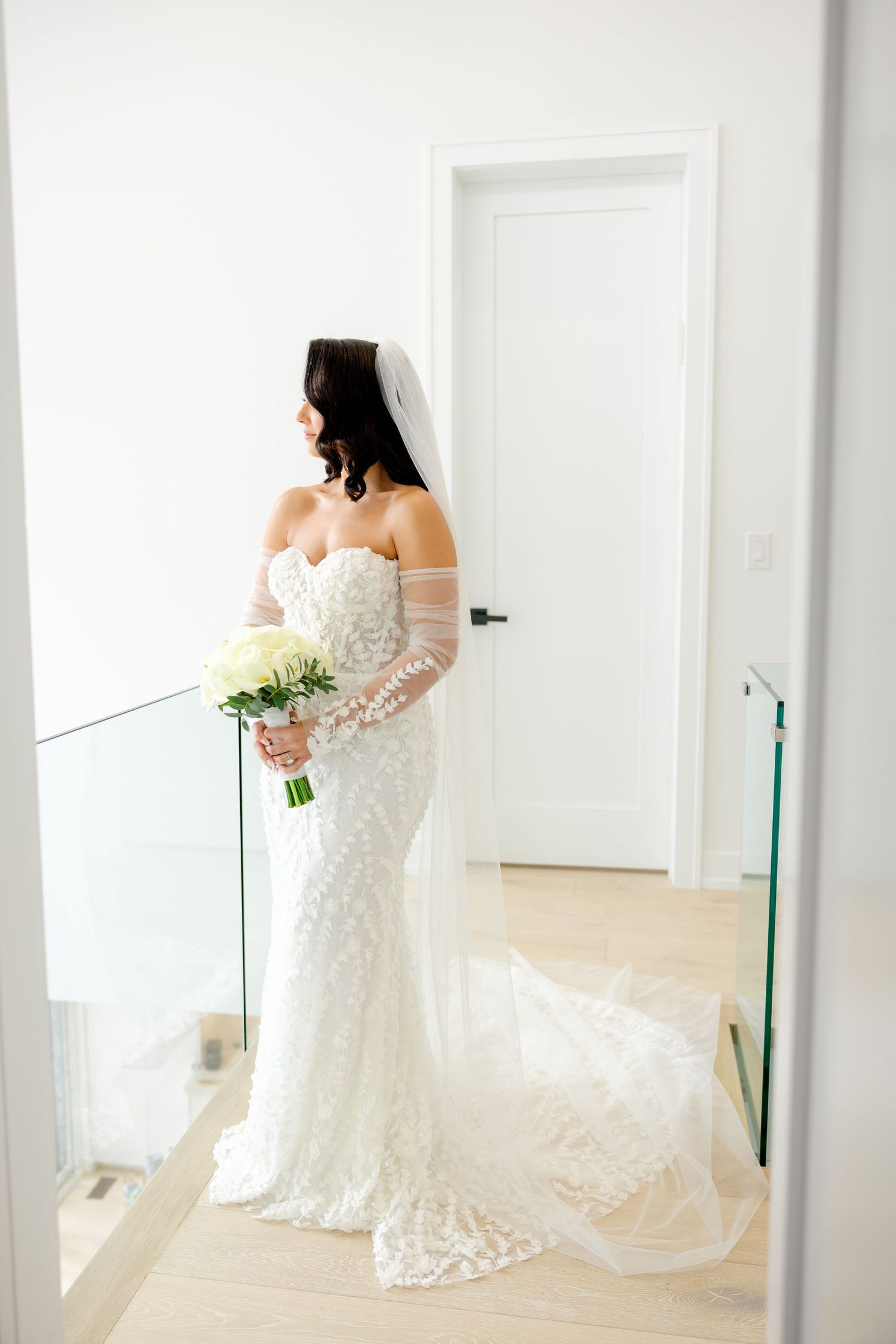 Elegant bridal portrait featuring a fitted lace gown and trailing veil in modern white hallway.