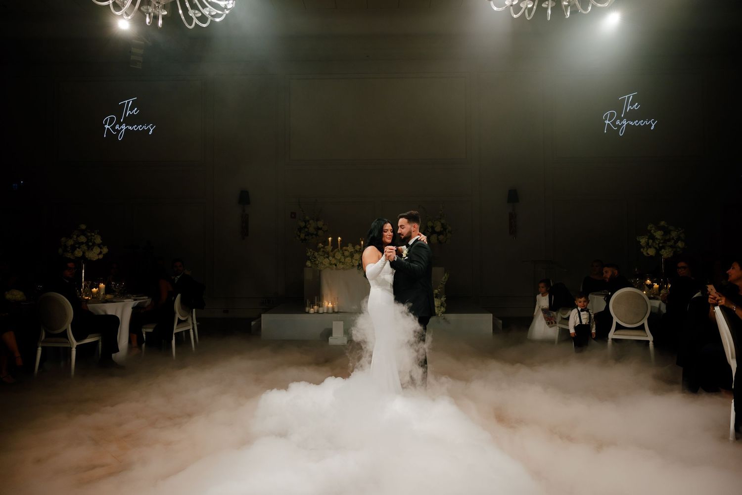 Dramatic lighting illuminates couple's dance through ethereal fog during wedding reception.