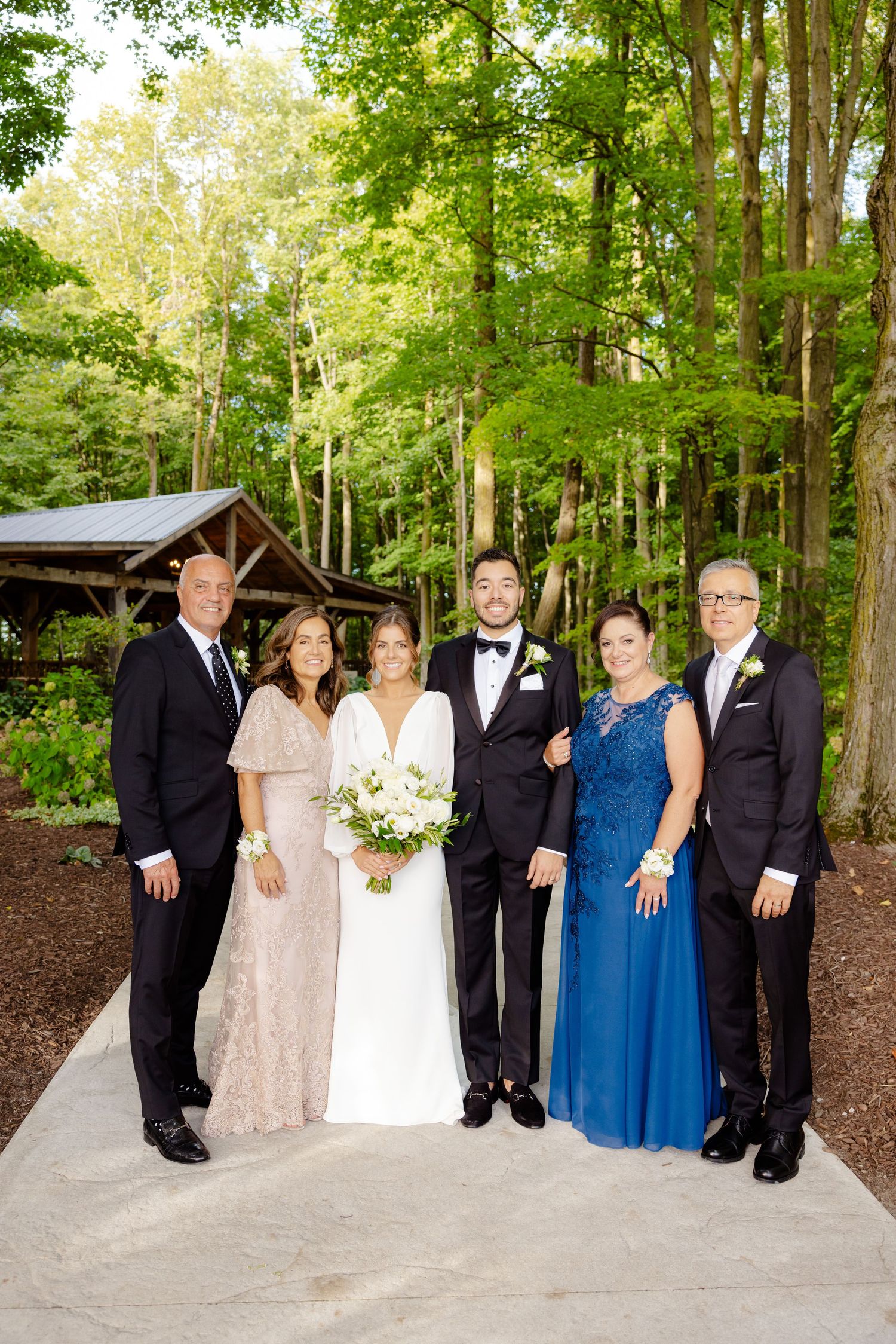 Elegant wedding group photo with family members in formal attire standing on garden pathway.