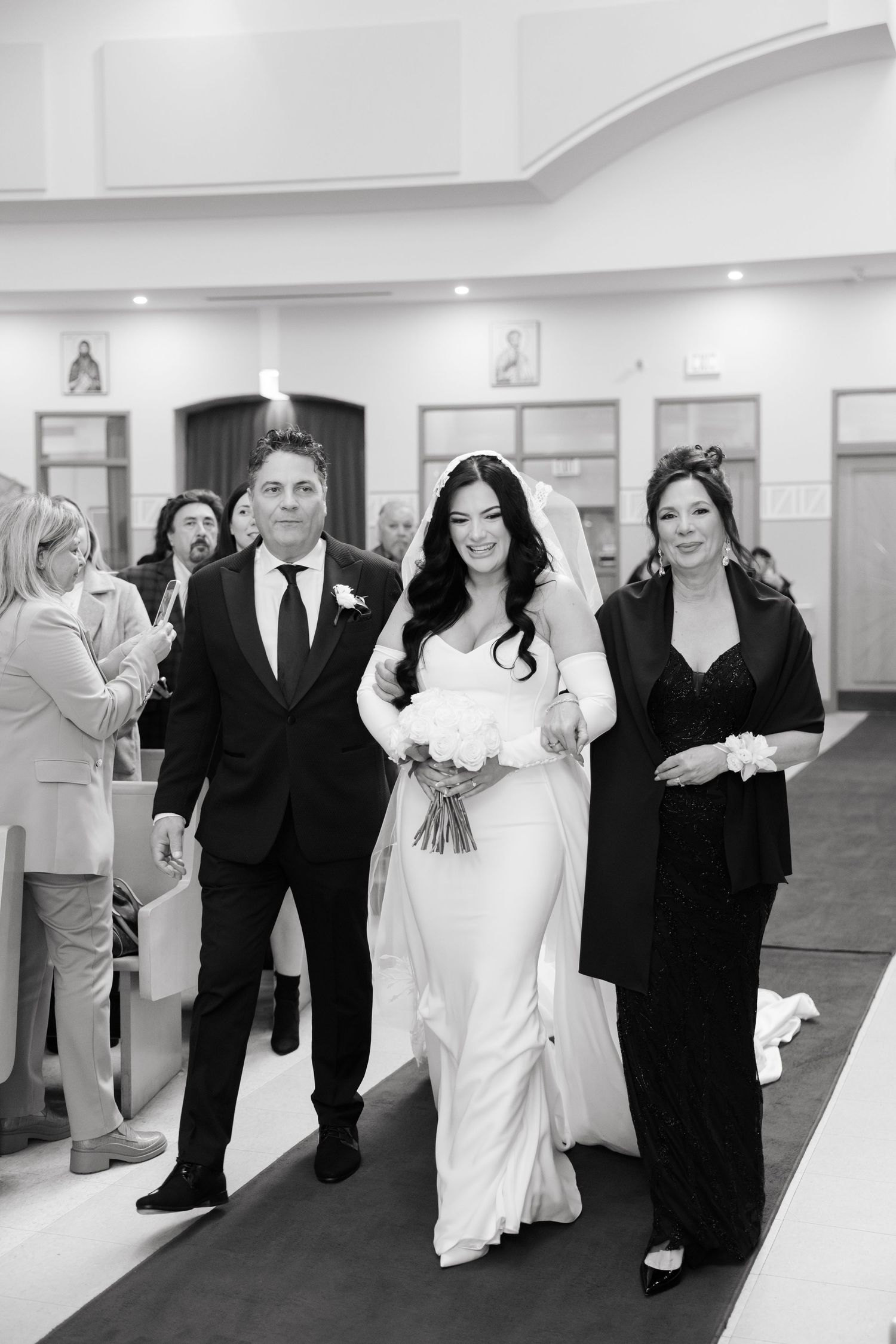 A black and white photo captures a wedding processional in a church hallway.