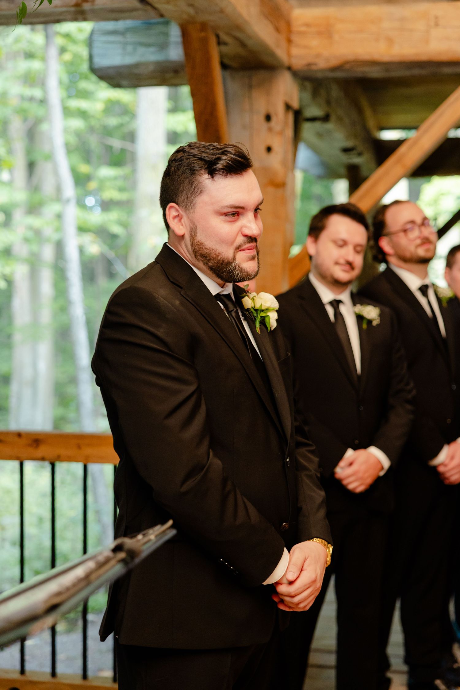 Groomsmen standing at altar in dark suits during outdoor forest wedding ceremony.