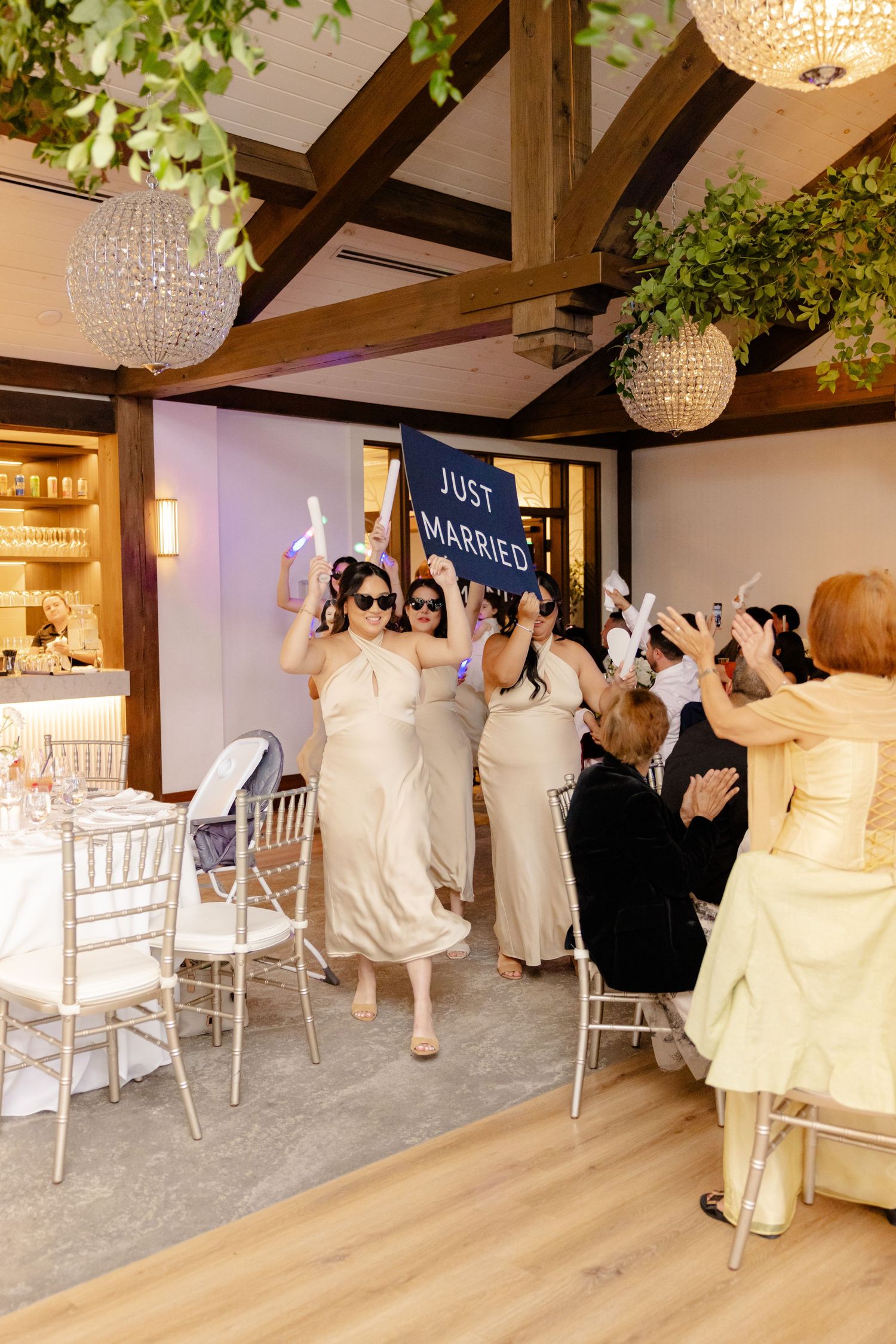 Wedding party celebrating in an elegant venue with crystal chandeliers and wooden beams.
