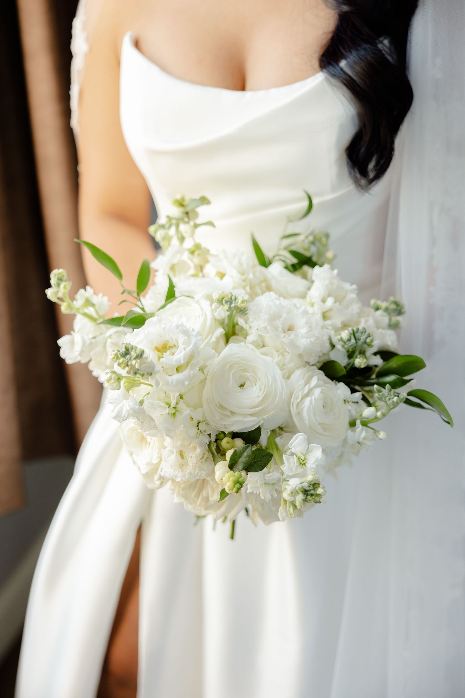 Close-up of white bridal bouquet with roses and delicate greenery against clean white wedding dress.