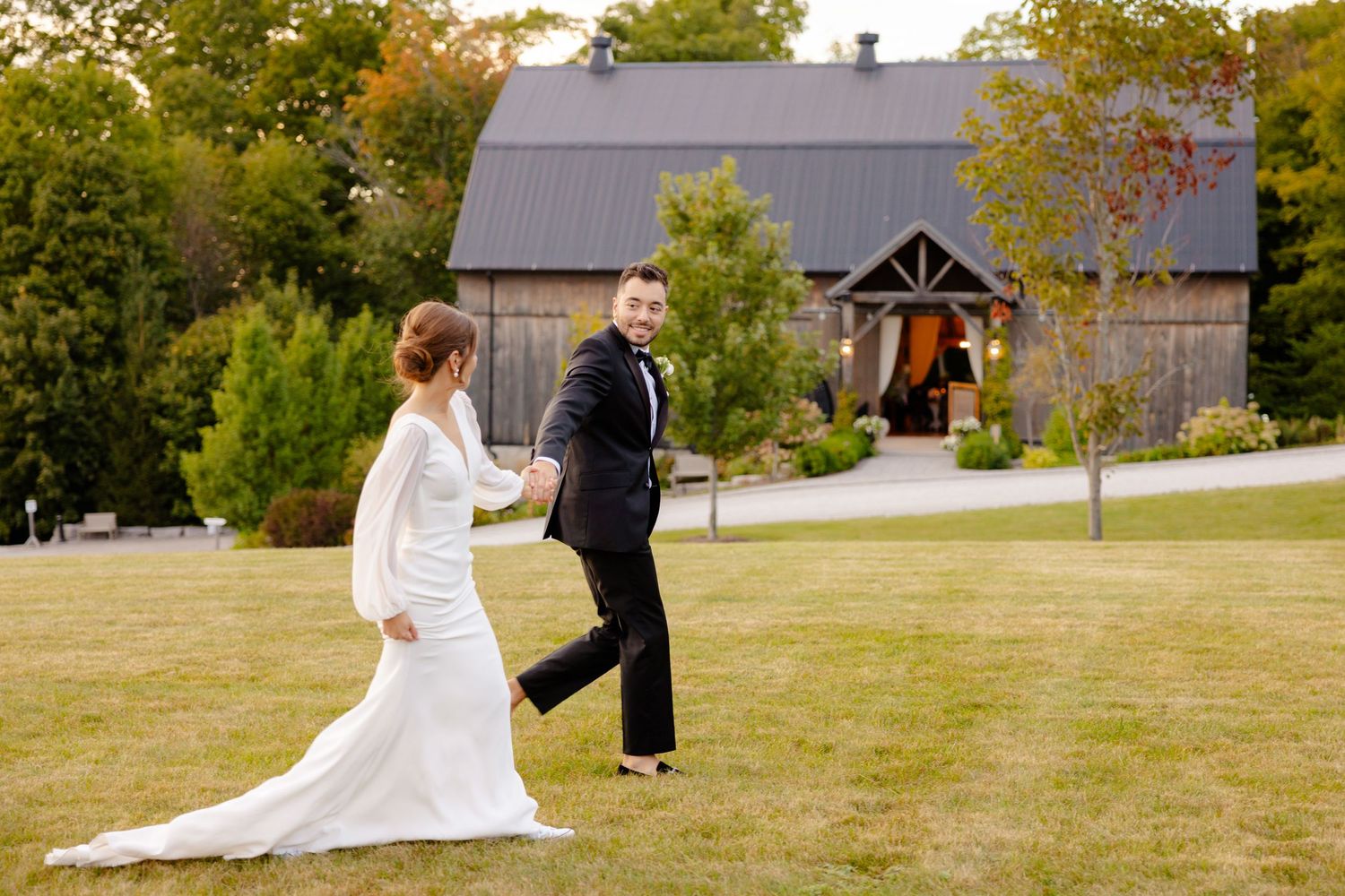 A couple walking together on their wedding day with a rustic barn venue behind them.
