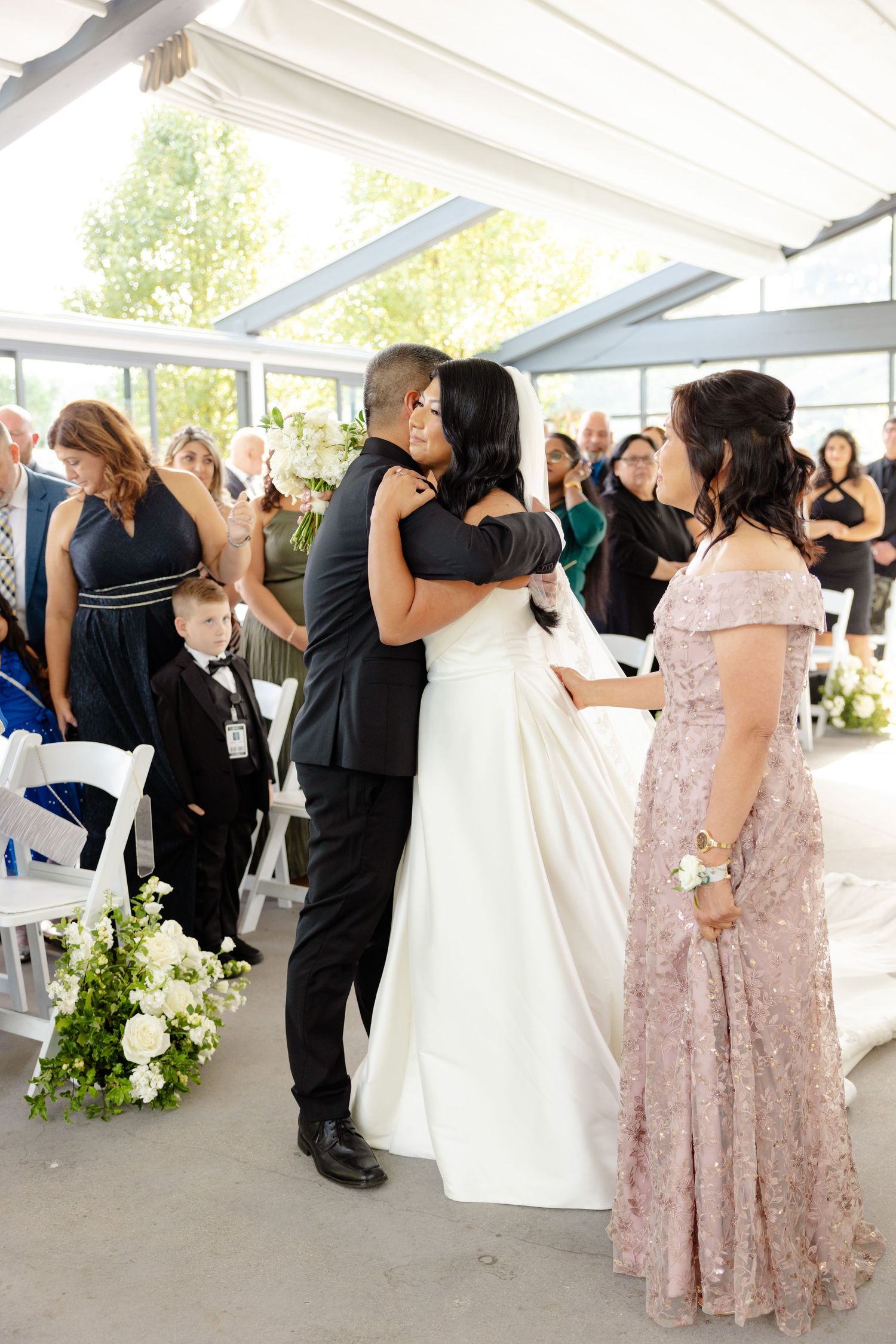 Emotional wedding ceremony moment in a light-filled venue with white decor.