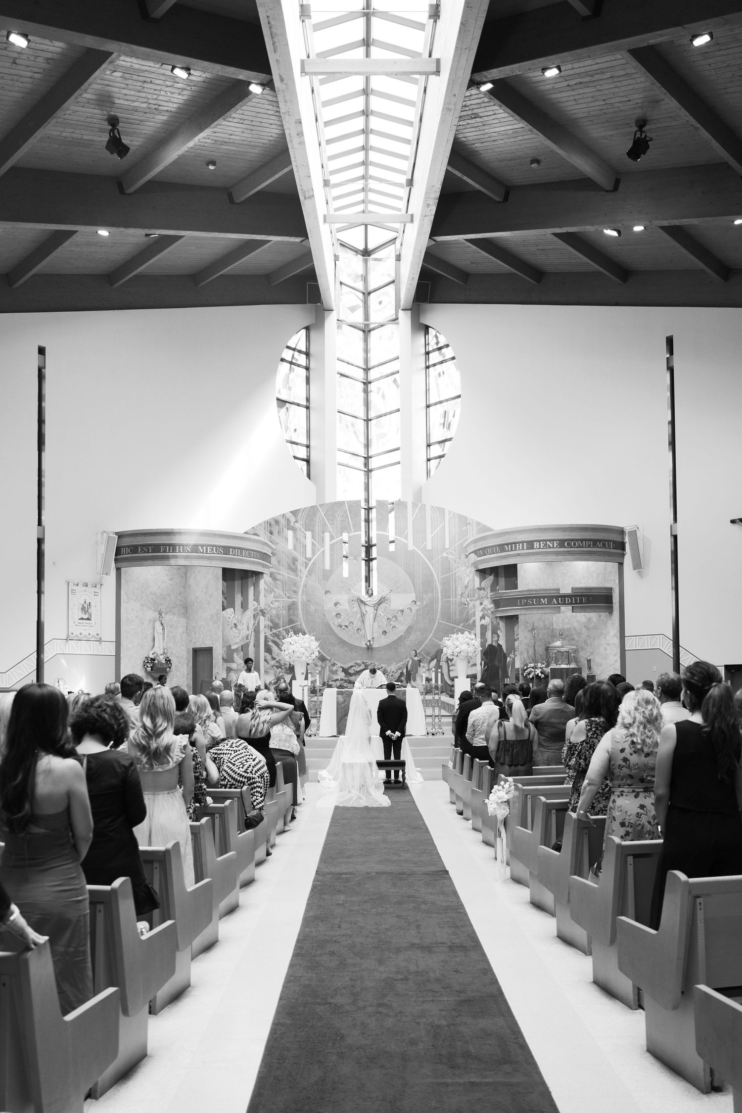 A black and white wide shot of a church wedding ceremony with guests seated in pews.
