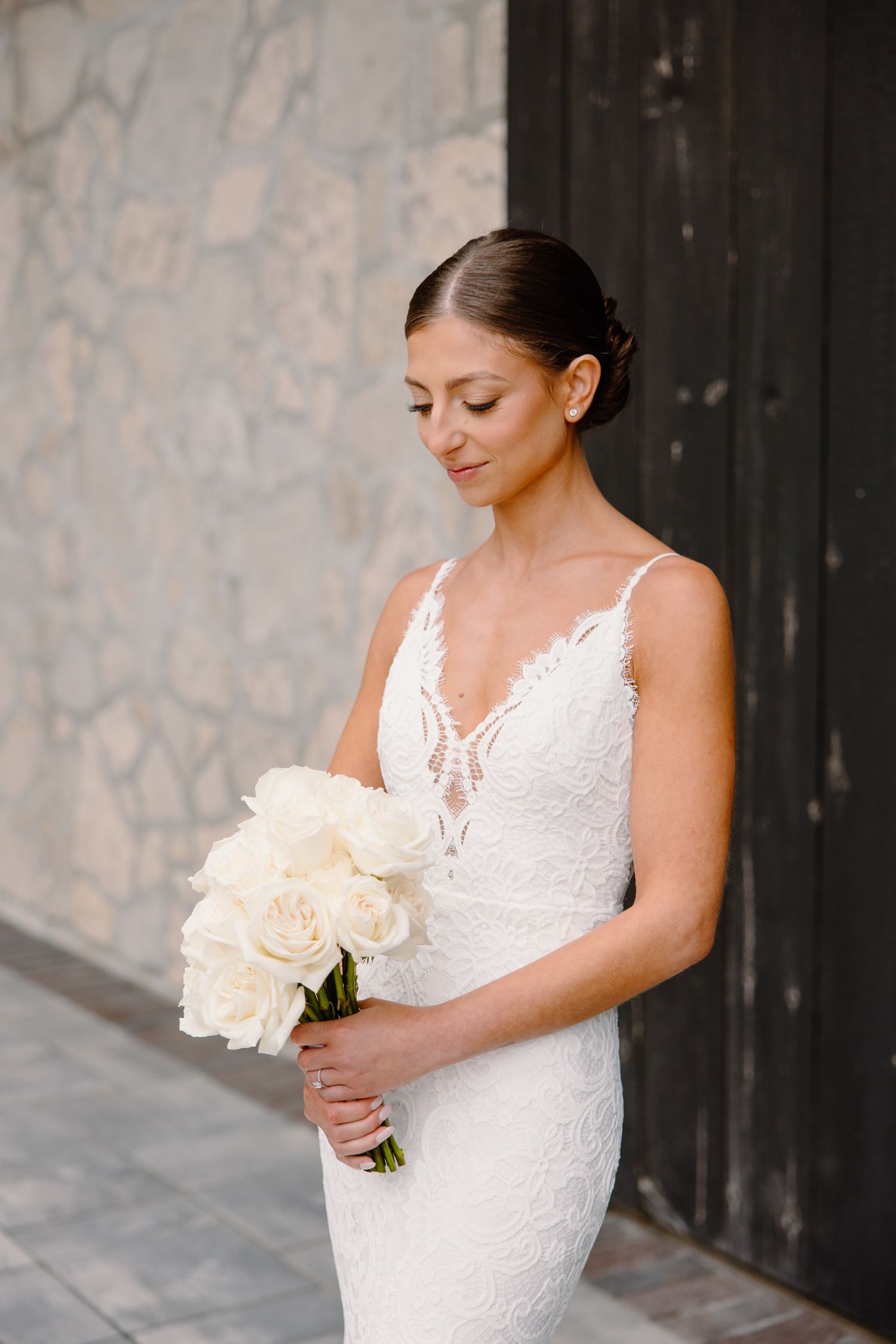 Elegant bridal portrait with white peony bouquet against stone wall.