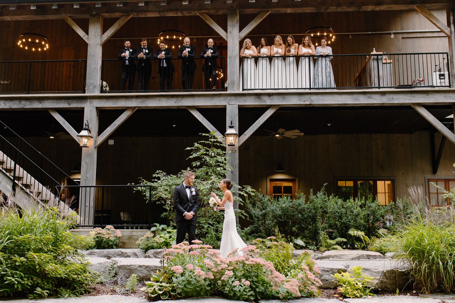 Wedding couple standing in front of rustic wooden pavilion surrounded by landscaped gardens.