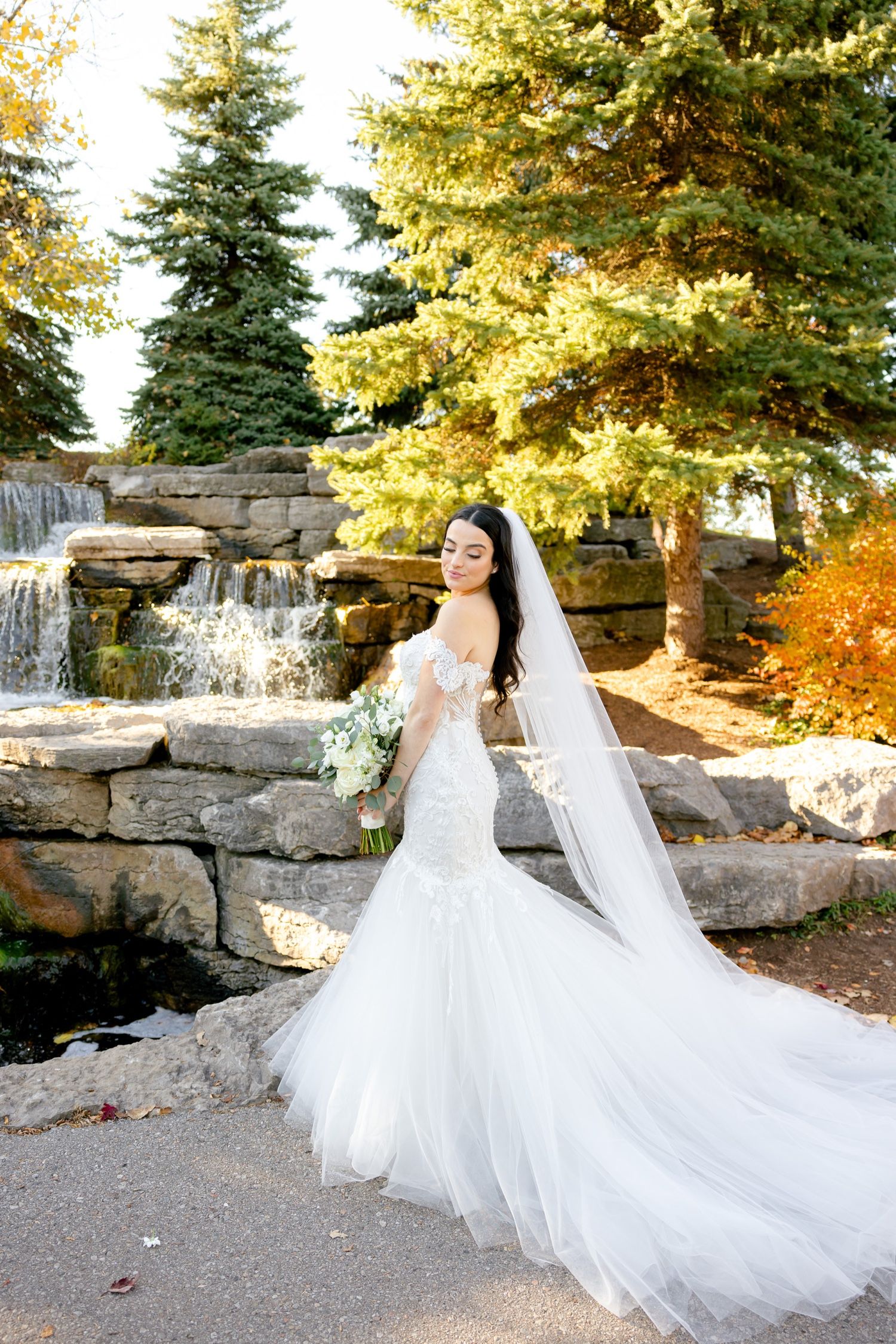A stunning bridal portrait featuring a flowing white gown against a waterfall and autumn scenery.