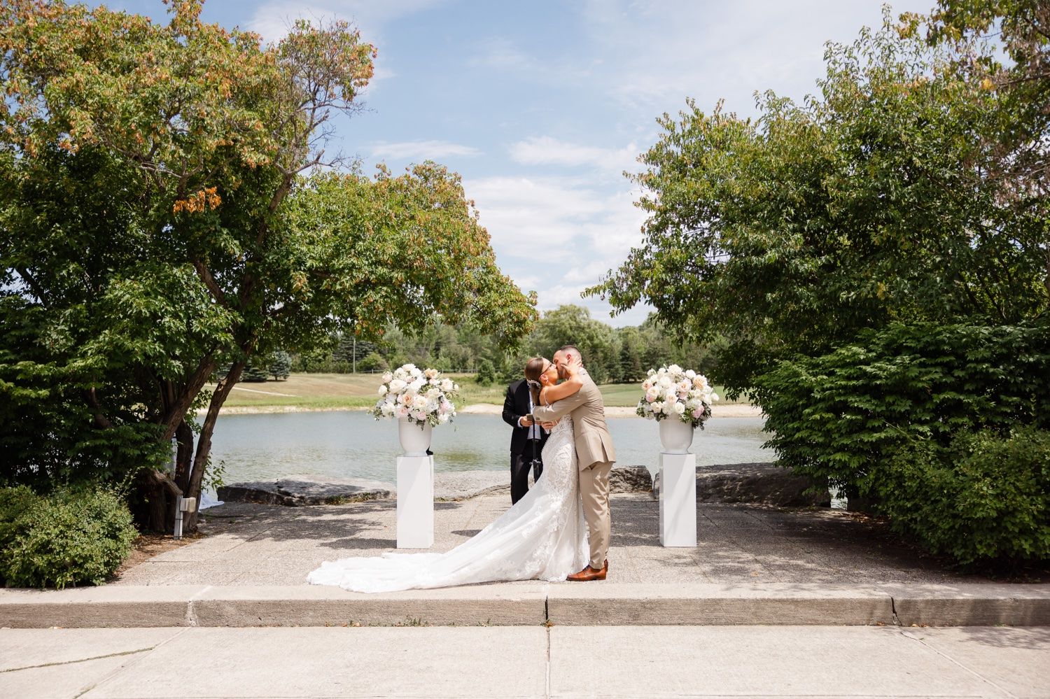 Wedding party poses at an elegant outdoor venue with lush greenery and white floral arrangements.