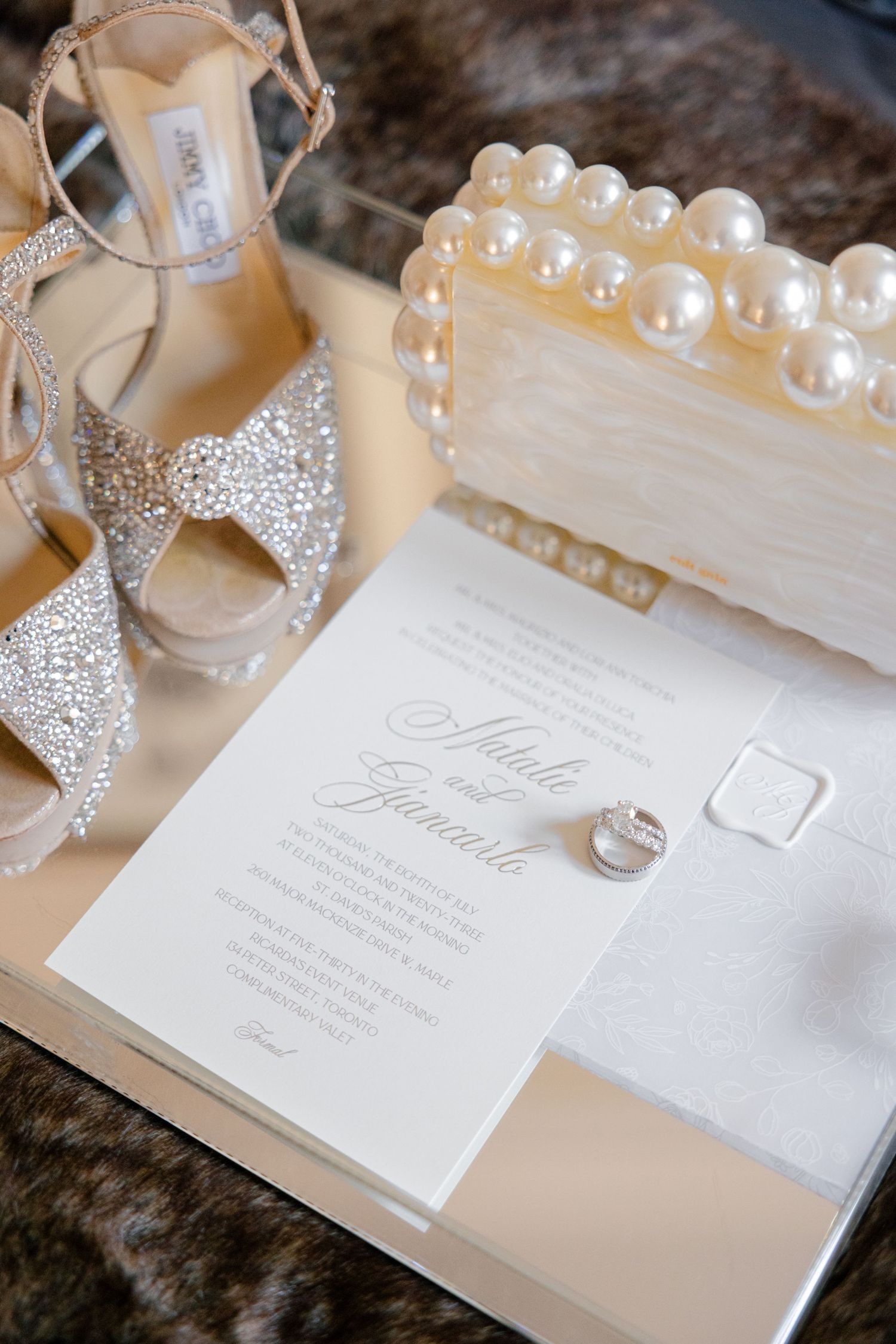 Wedding invitation with sparkly bridal shoes and pearl details on textured background.
