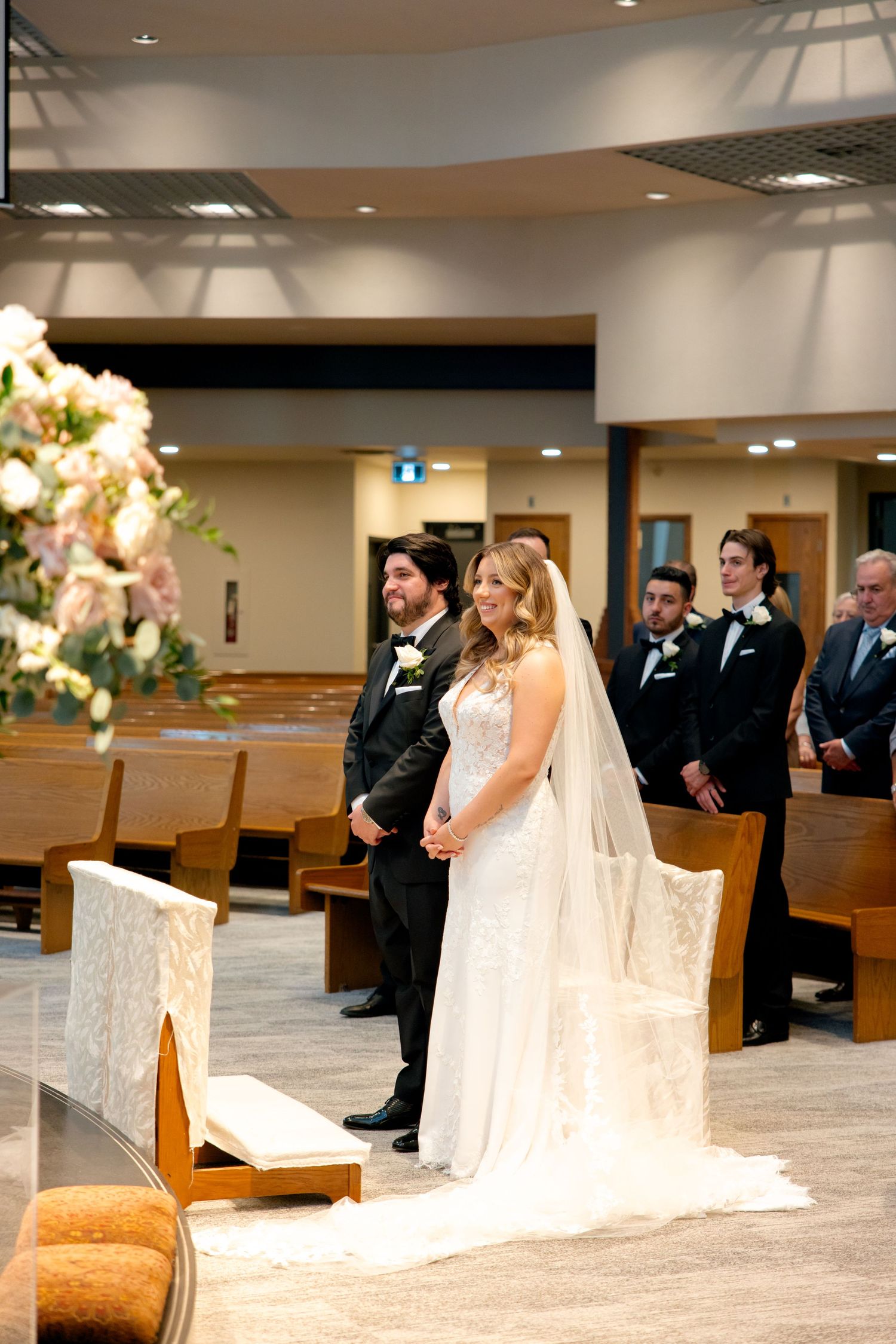 A couple exchanges vows during their wedding ceremony in a modern church sanctuary with floral arrangements.