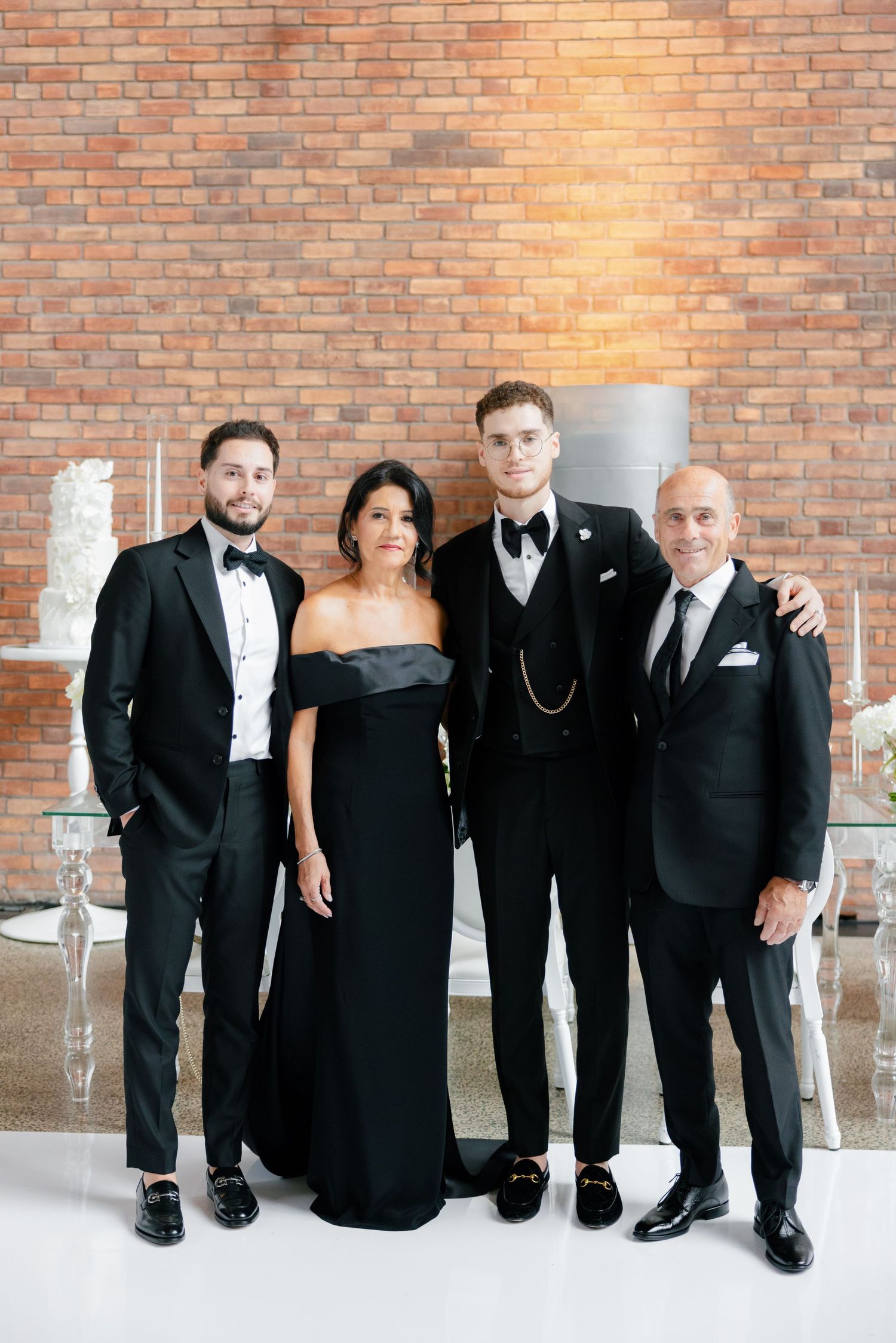 Four people in formal attire pose together at a wedding reception with exposed brick wall backdrop.