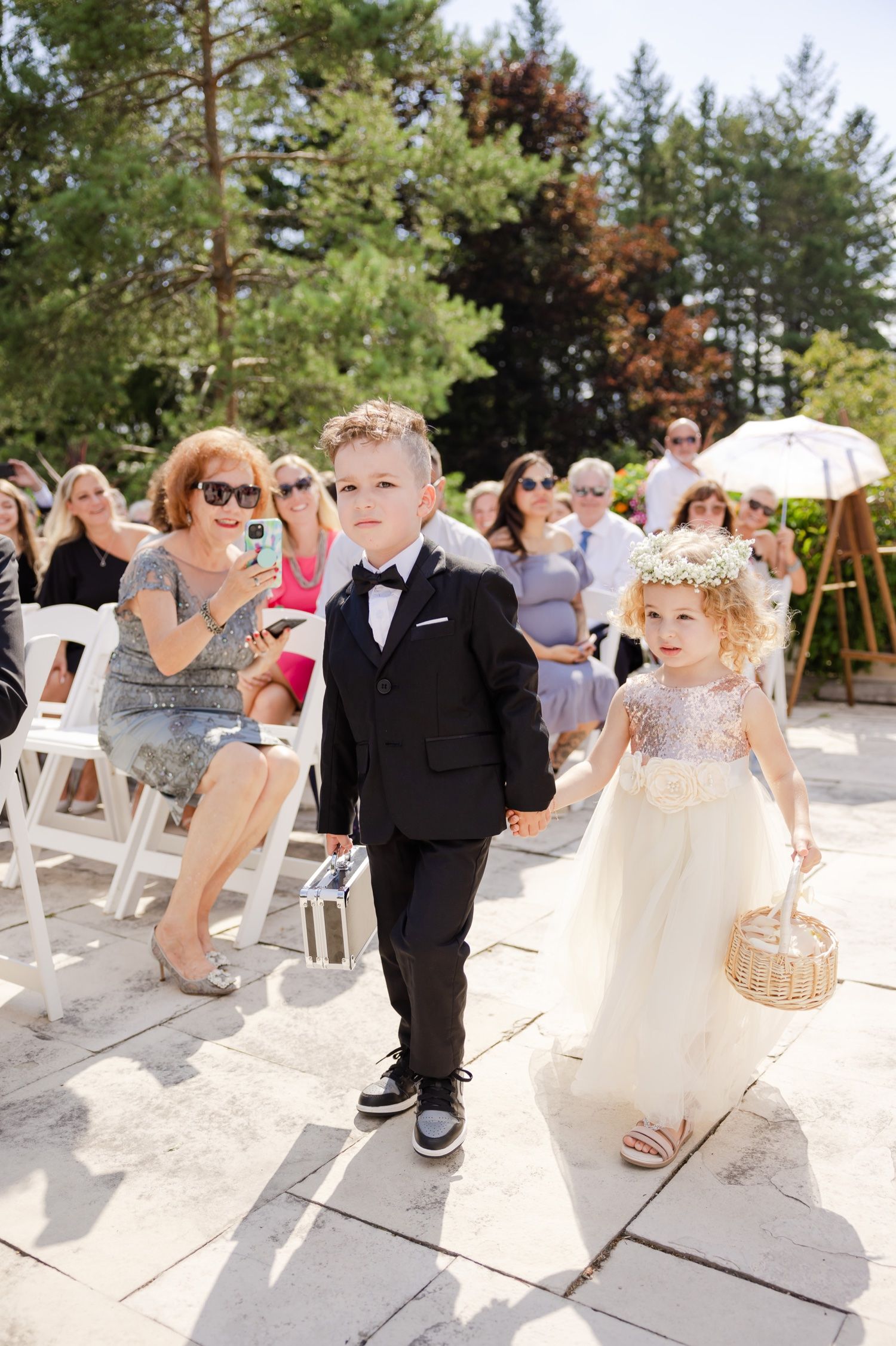 Ring bearer and flower girl walking down aisle at outdoor wedding ceremony.