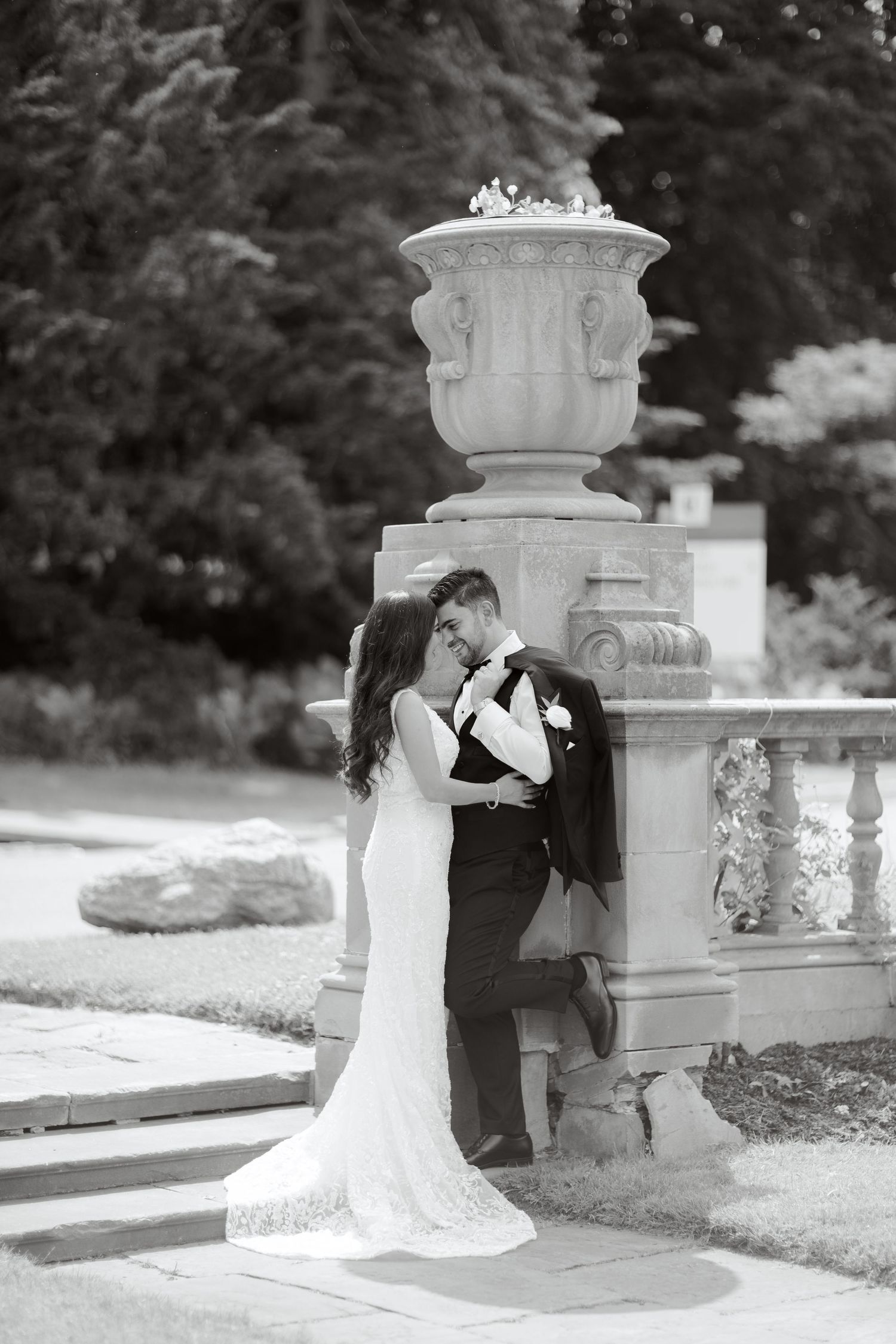 A wedding couple in formal attire poses against a classic stone column outdoors.