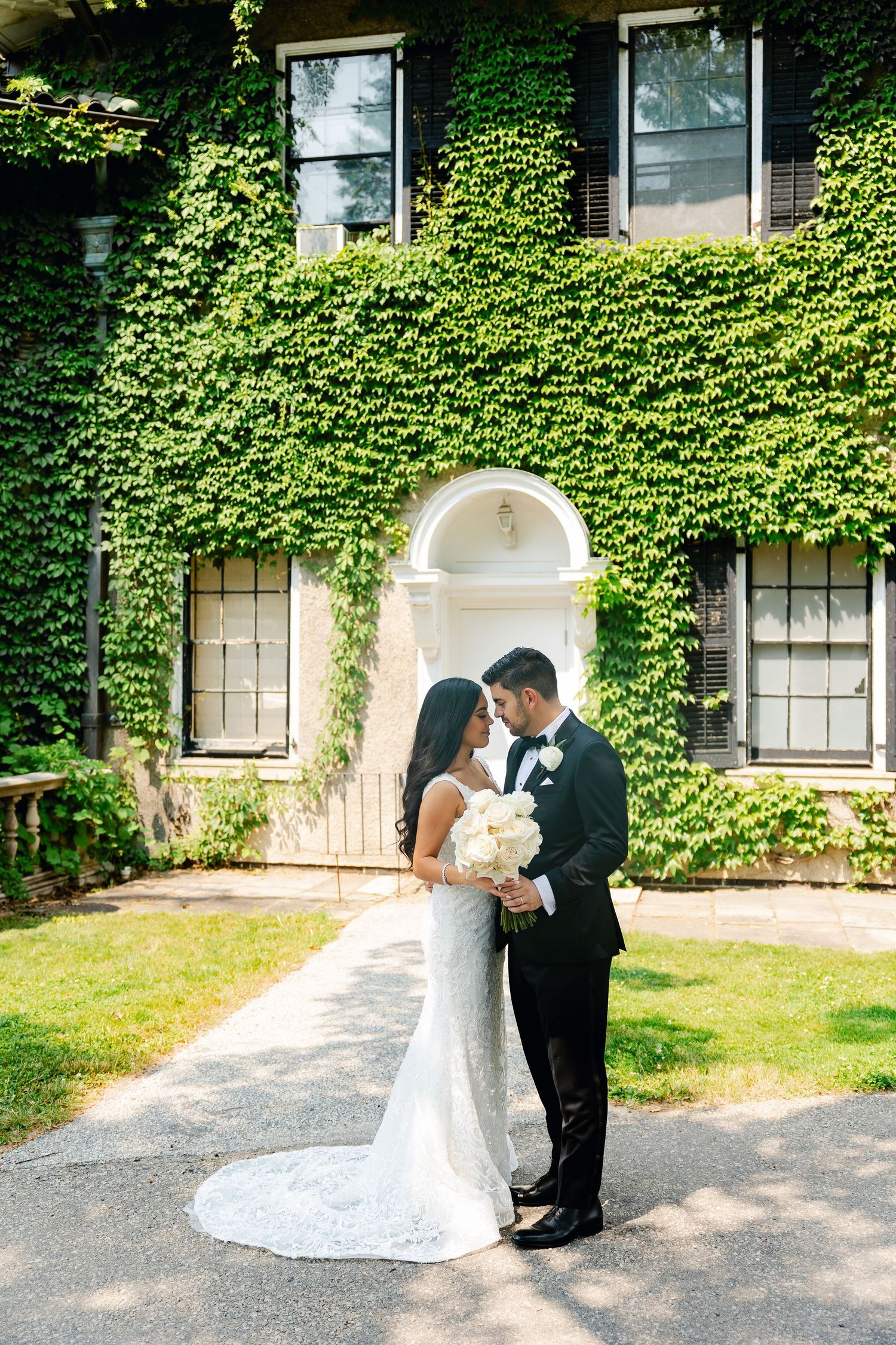 A romantic wedding photo in front of an ivy-covered building with a white arched doorway.