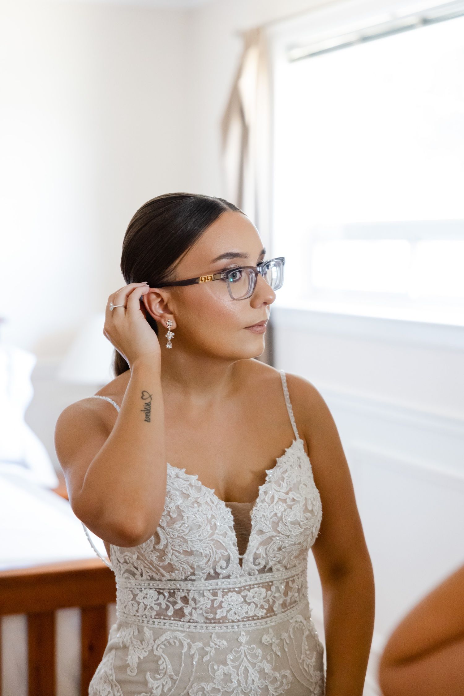 Elegant bridal portrait showing delicate lace details and glasses in natural window light.
