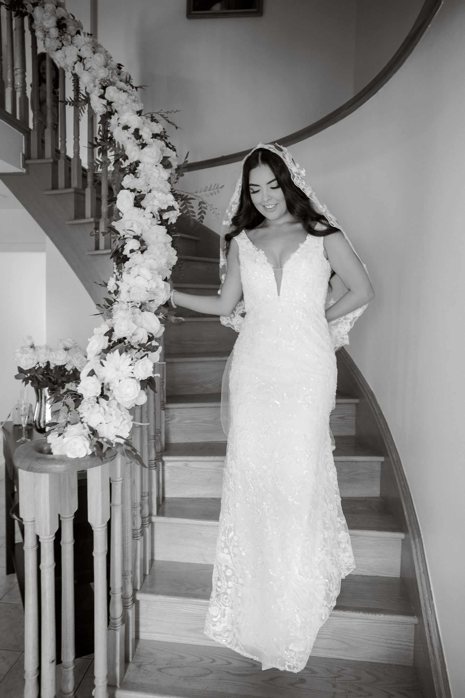 Black and white photo of bride on staircase with floral decorations.