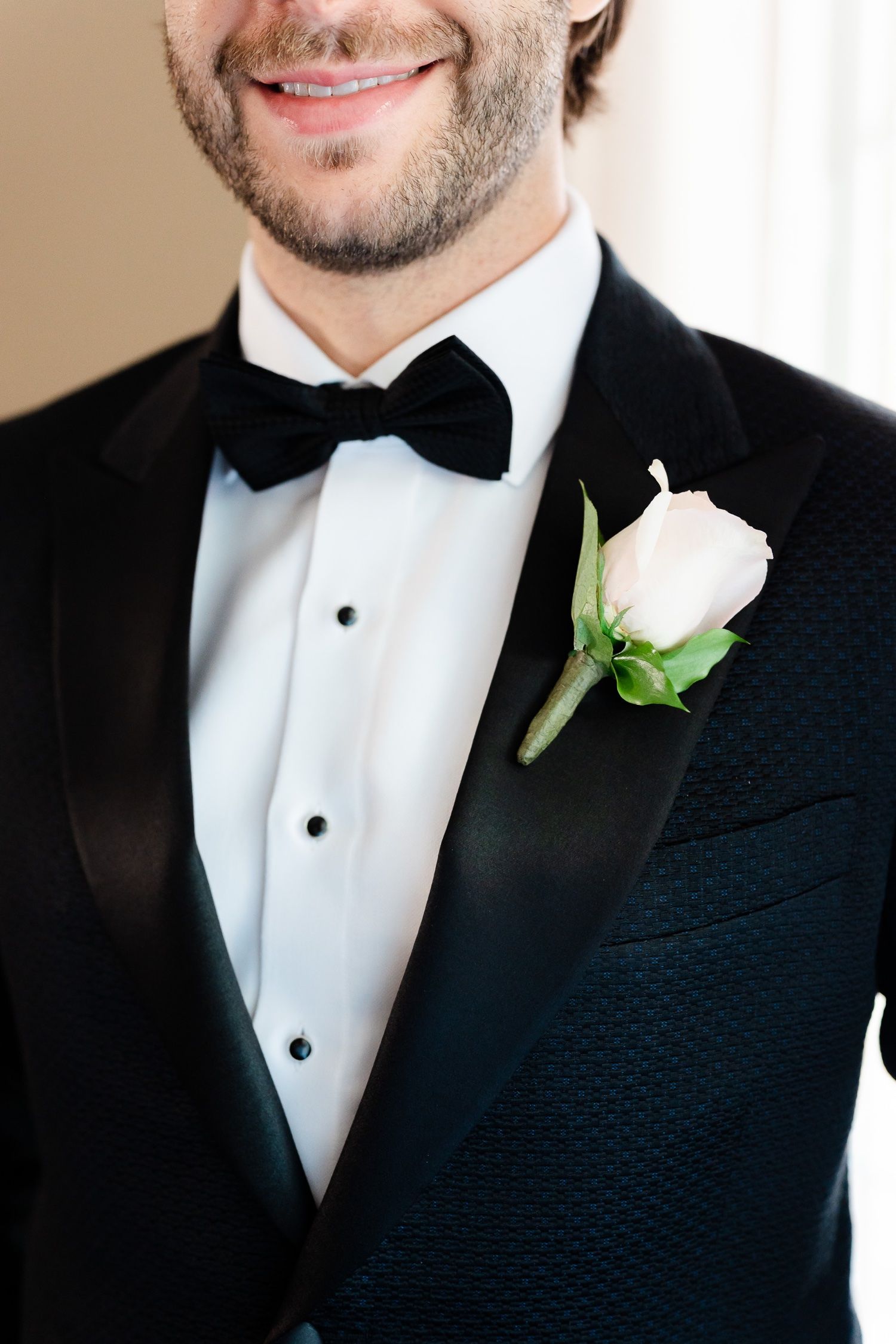 Detail shot of black bowtie and white rose boutonniere on formal tuxedo.