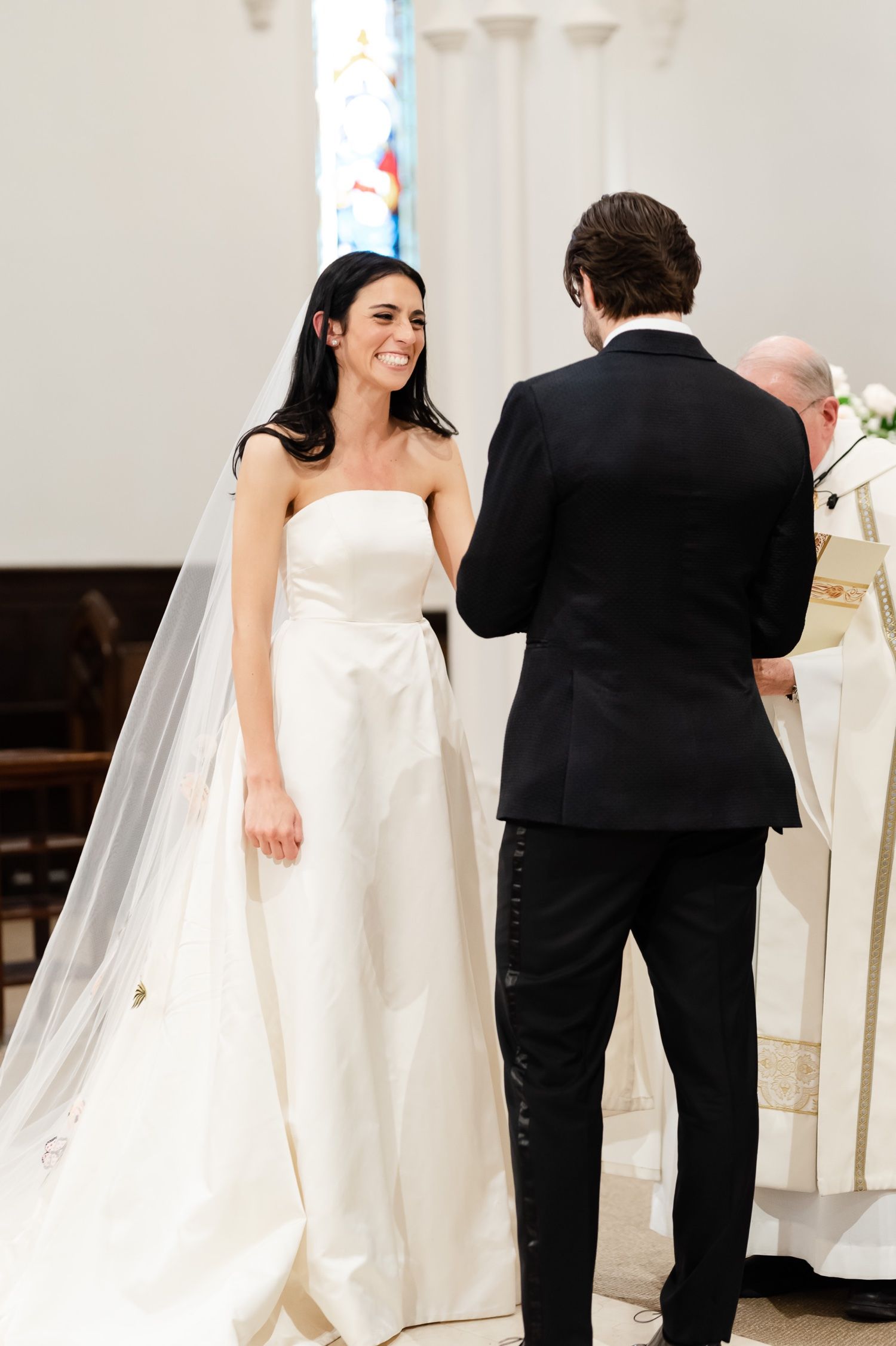 Wedding ceremony in progress at an elegant church altar with white columns and stained glass.