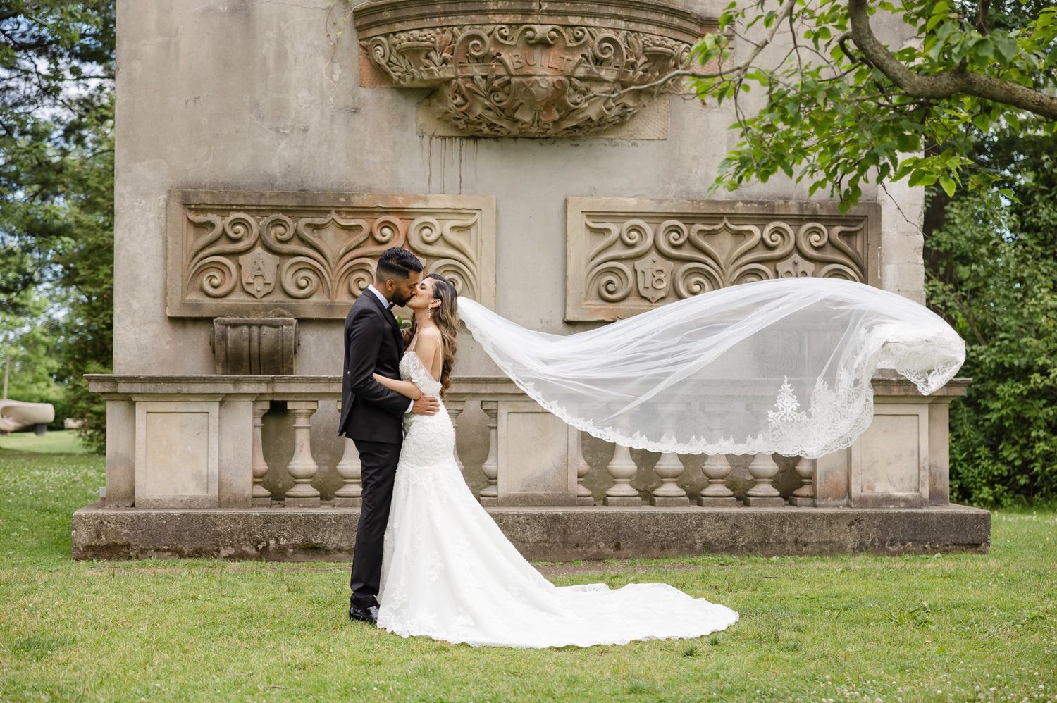 A dramatic wedding photo against ornate stone architecture with flowing veil in the breeze.