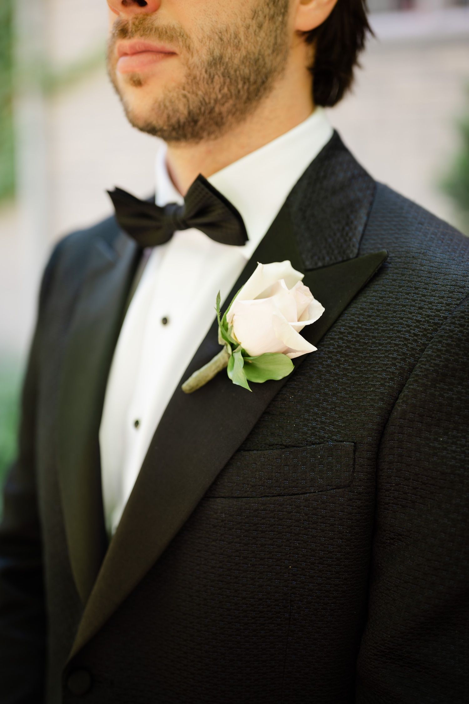 Close-up detail of black textured tuxedo with white rose boutonniere.