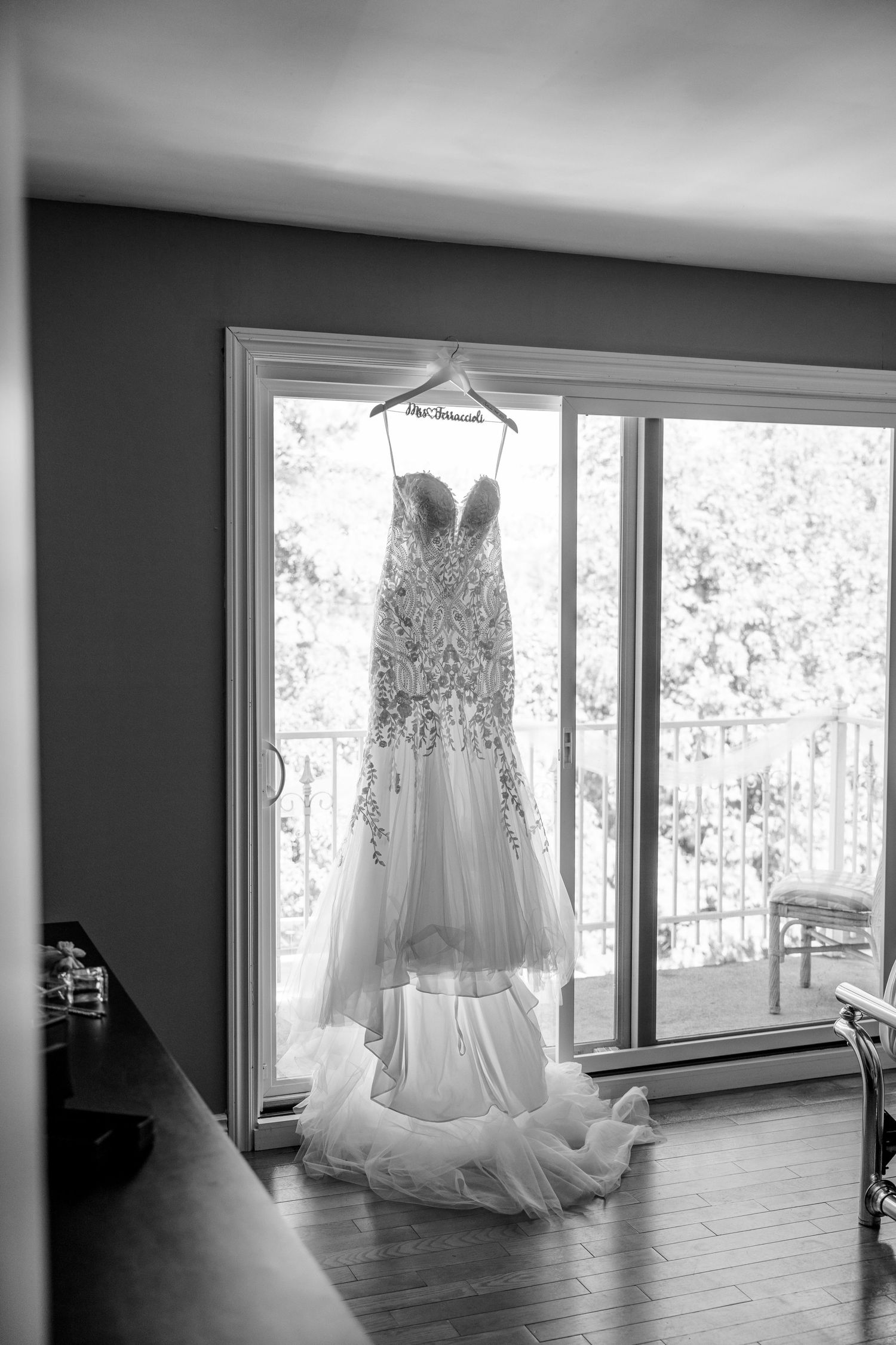 An elegant lace wedding gown with sweetheart neckline hanging in front of large windows in natural light.
