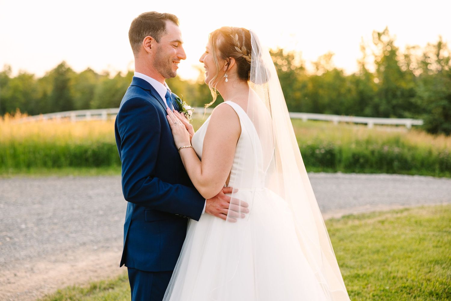 A newlywed couple embraces outdoors at sunset with a natural field in the background.