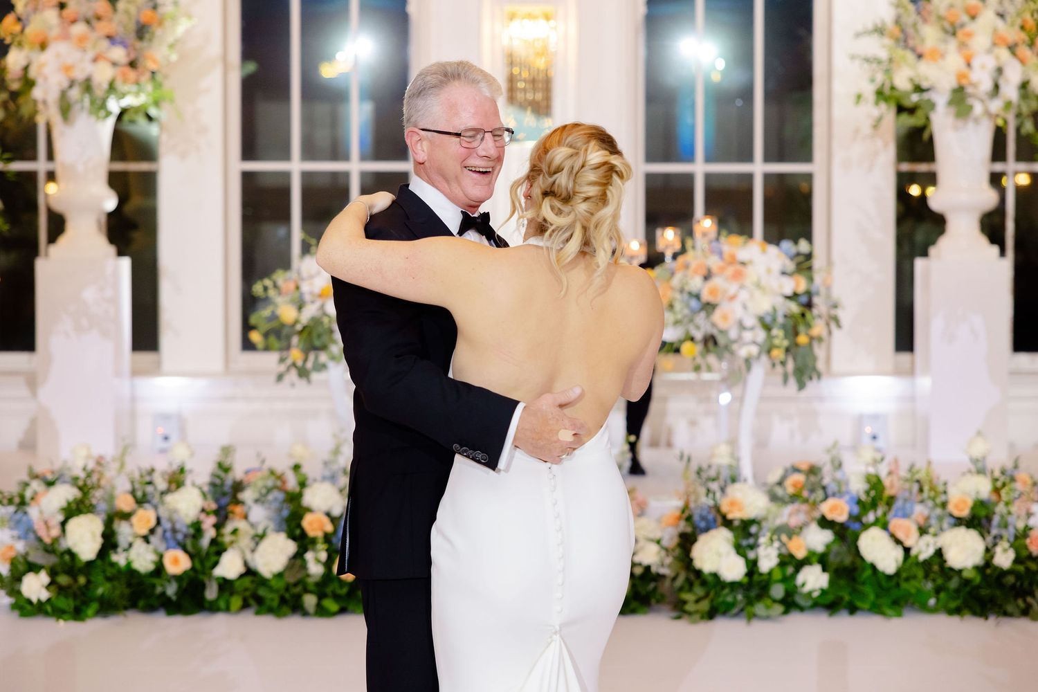 Wedding ceremony space decorated with white pedestals and romantic floral arrangements in a bright indoor venue.