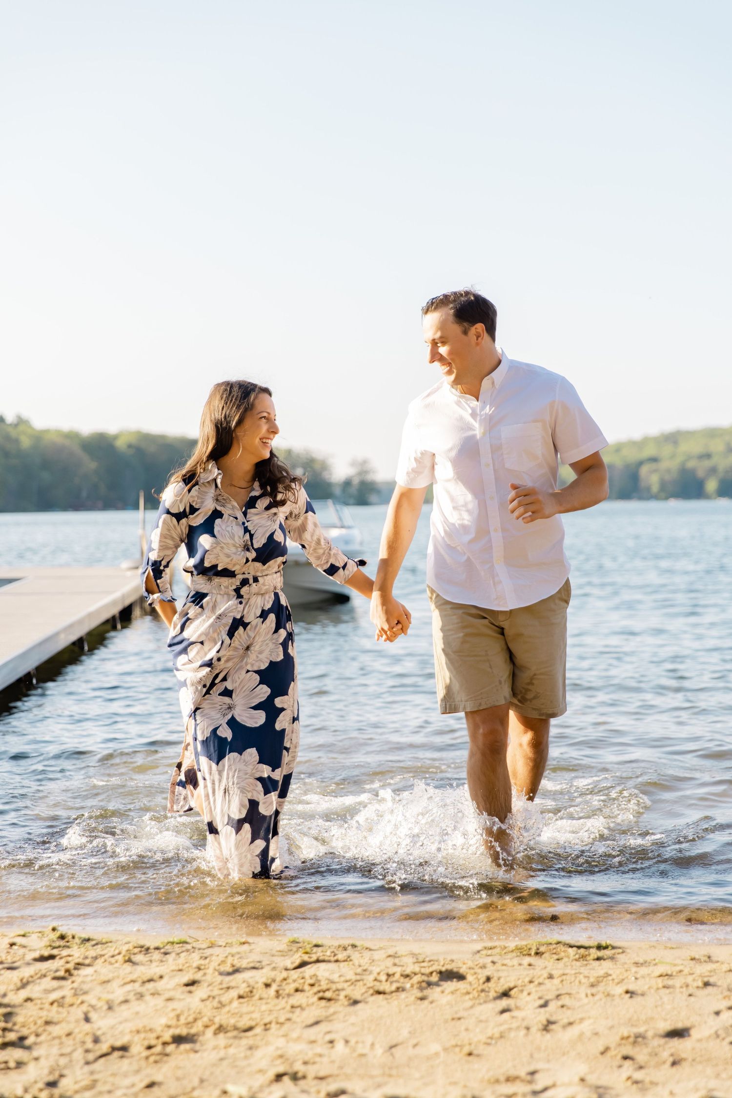 A couple runs playfully through the shallow water at a lake beach, splashing and laughing.
