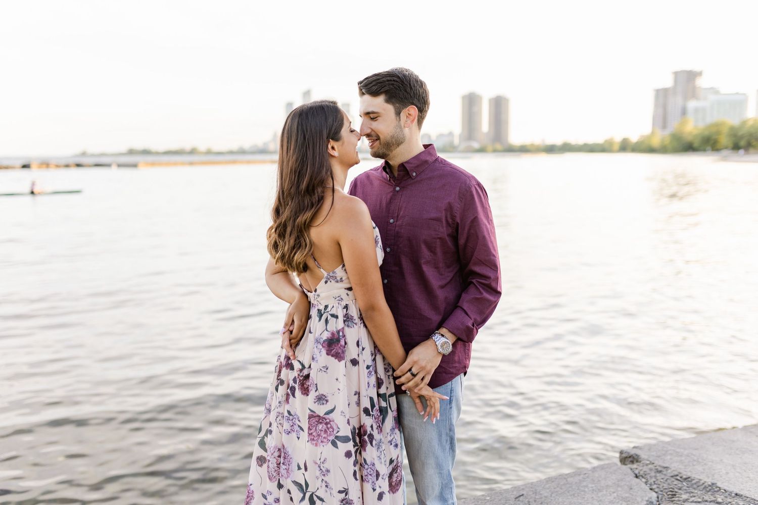 Couple in purple shirt and floral dress embracing near waterfront.