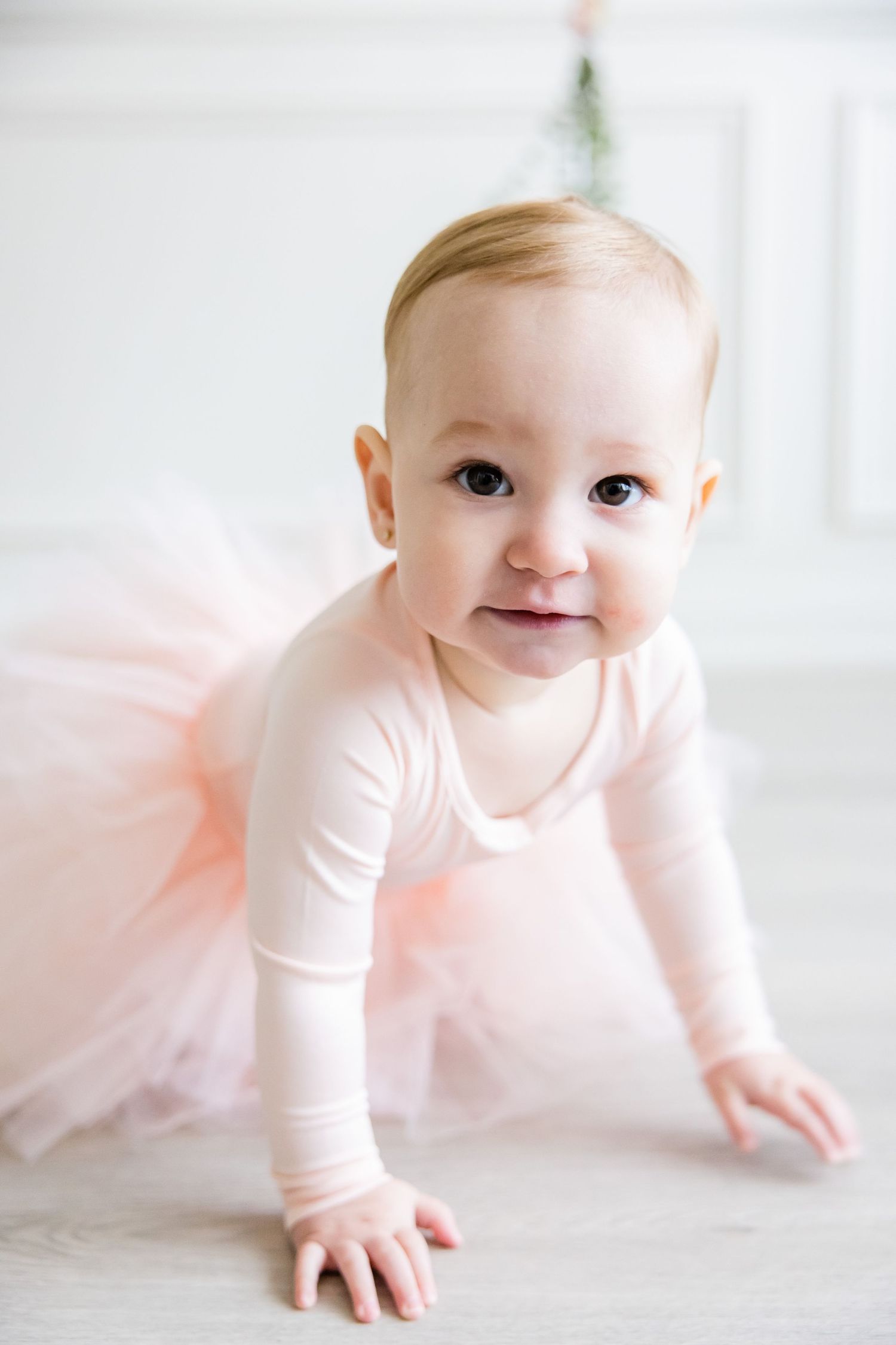 Close up of toddler in pink ballerina outfit crawling on light floor.