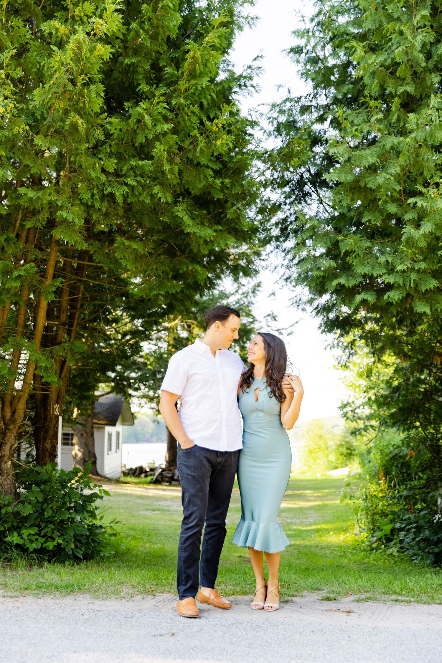 A couple in coordinating outfits embraces on a tree-lined pathway during golden hour.
