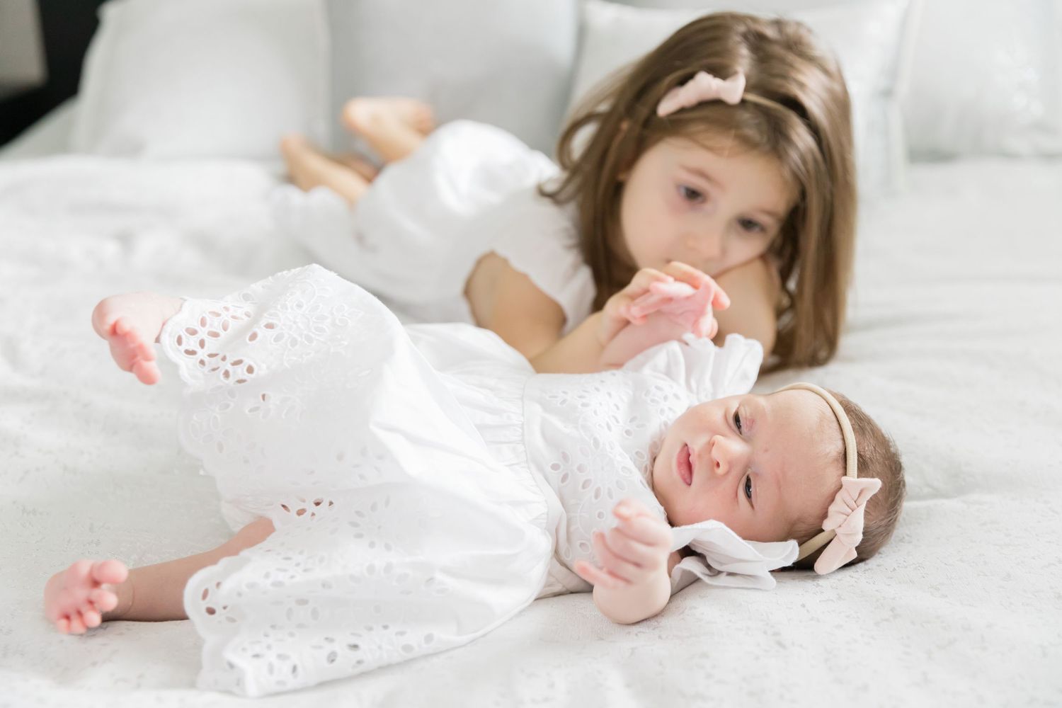 Two children in white dresses resting on white bedding.