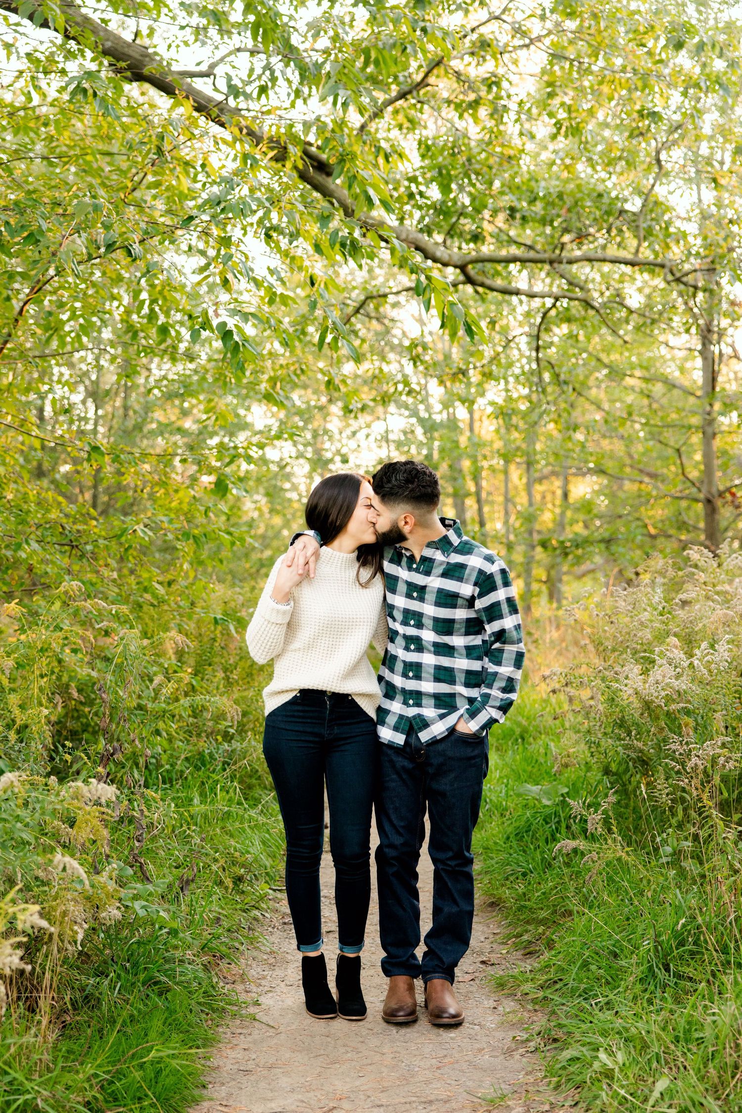Couple standing close together on dirt path surrounded by fall foliage.