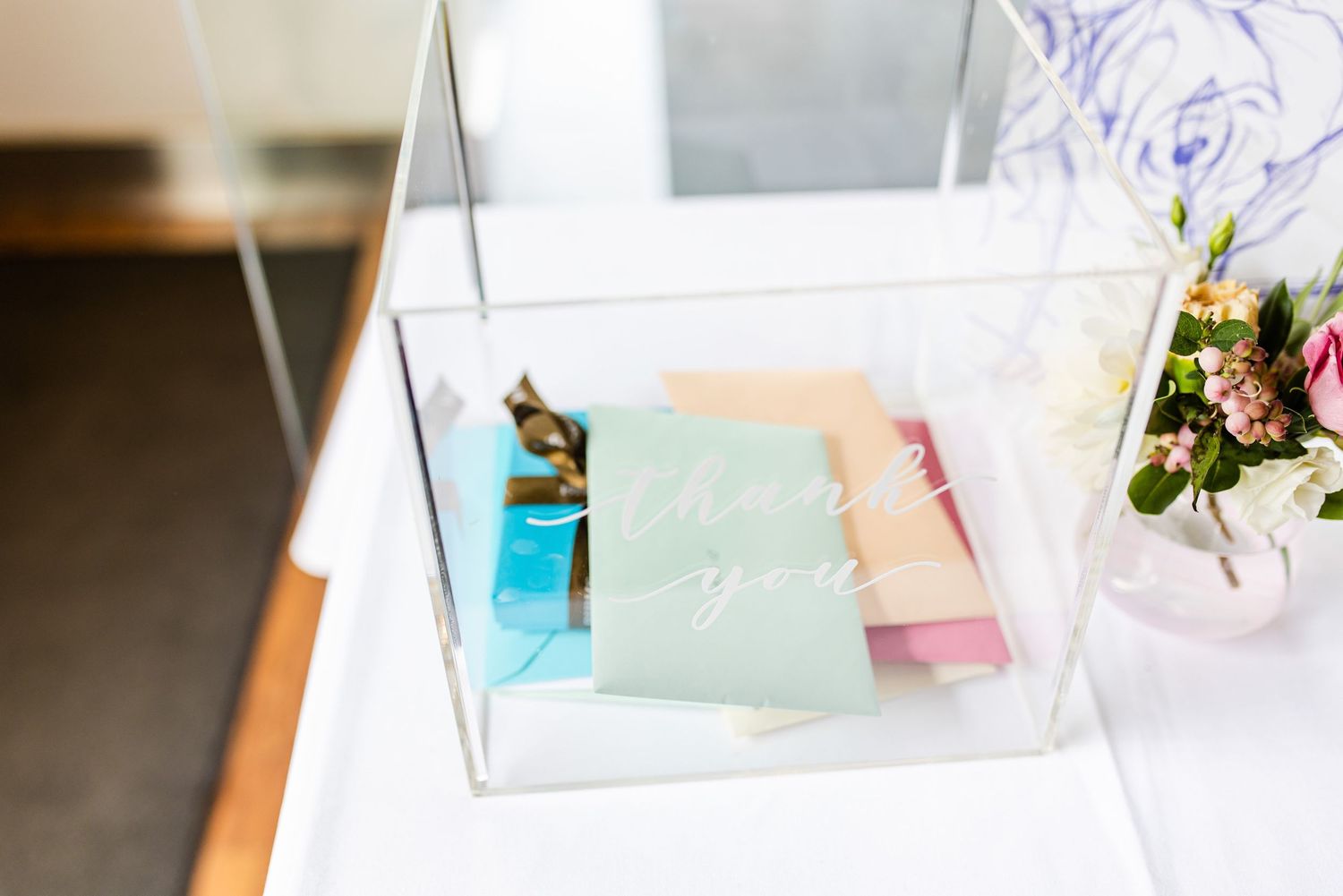 Pastel-colored cards and papers displayed in an acrylic box on a wooden surface with floral decor.