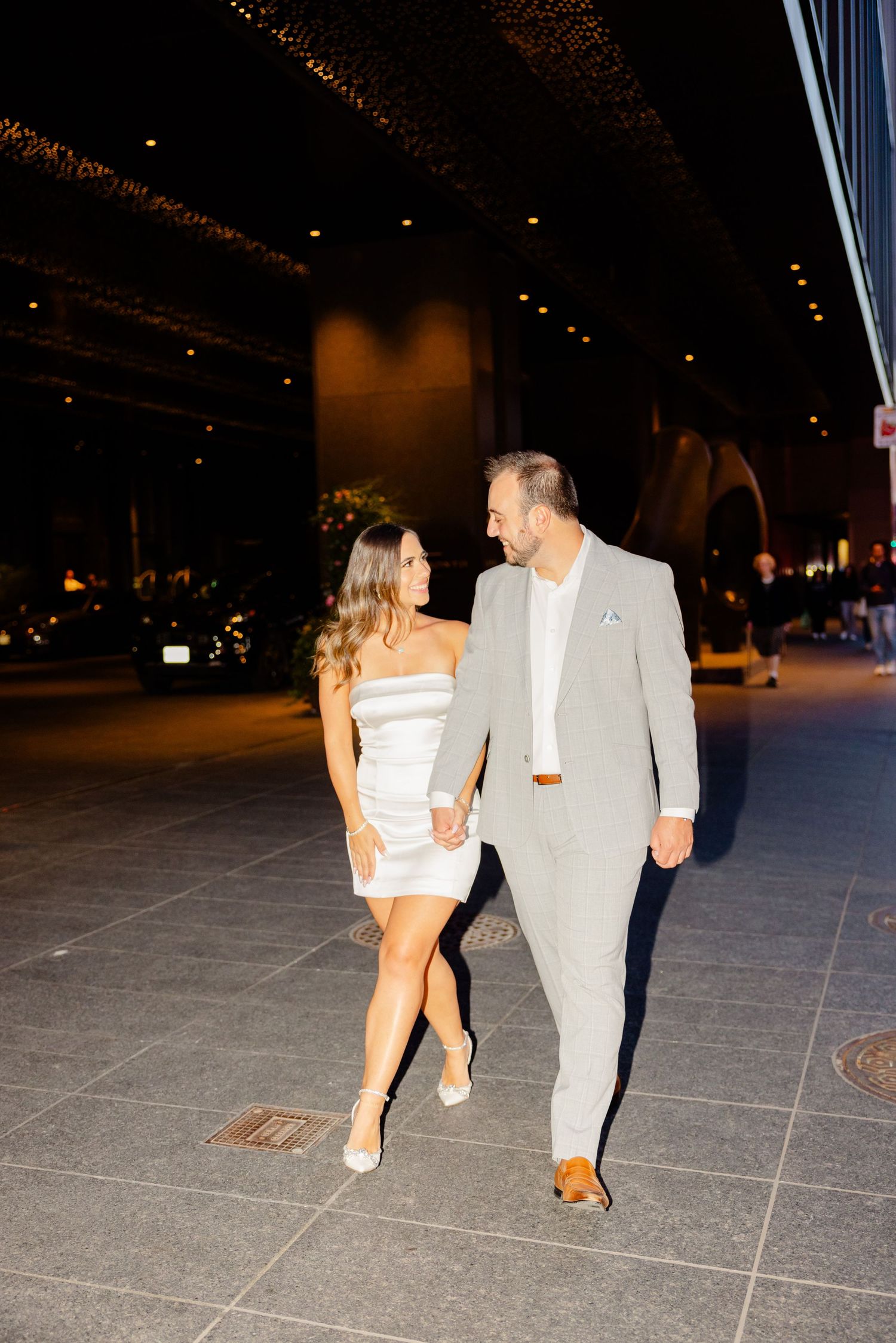 Elegant couple strolls together under illuminated overhead lighting.