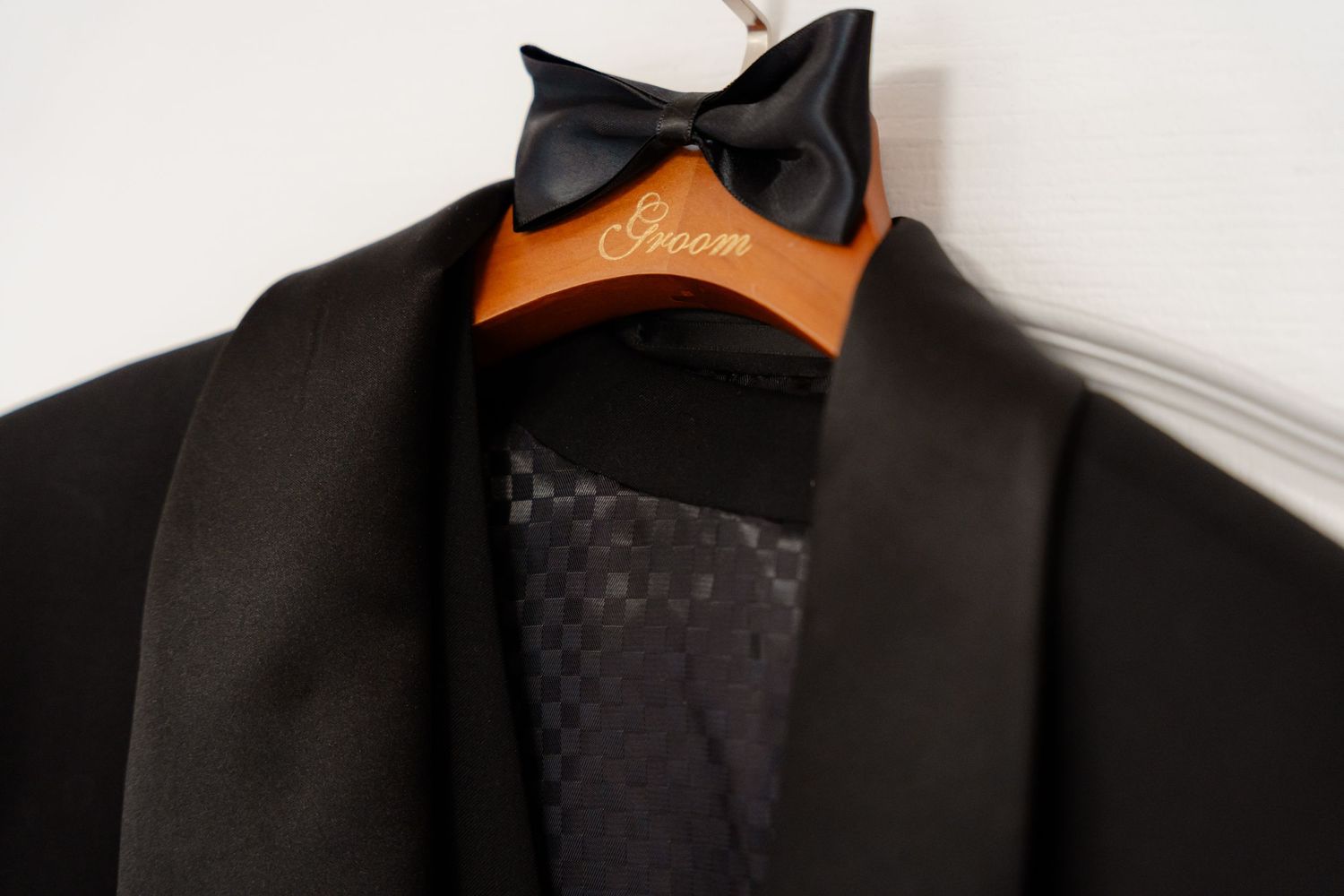 Close-up of black bow tie on wooden hanger with tuxedo jacket lapel.
