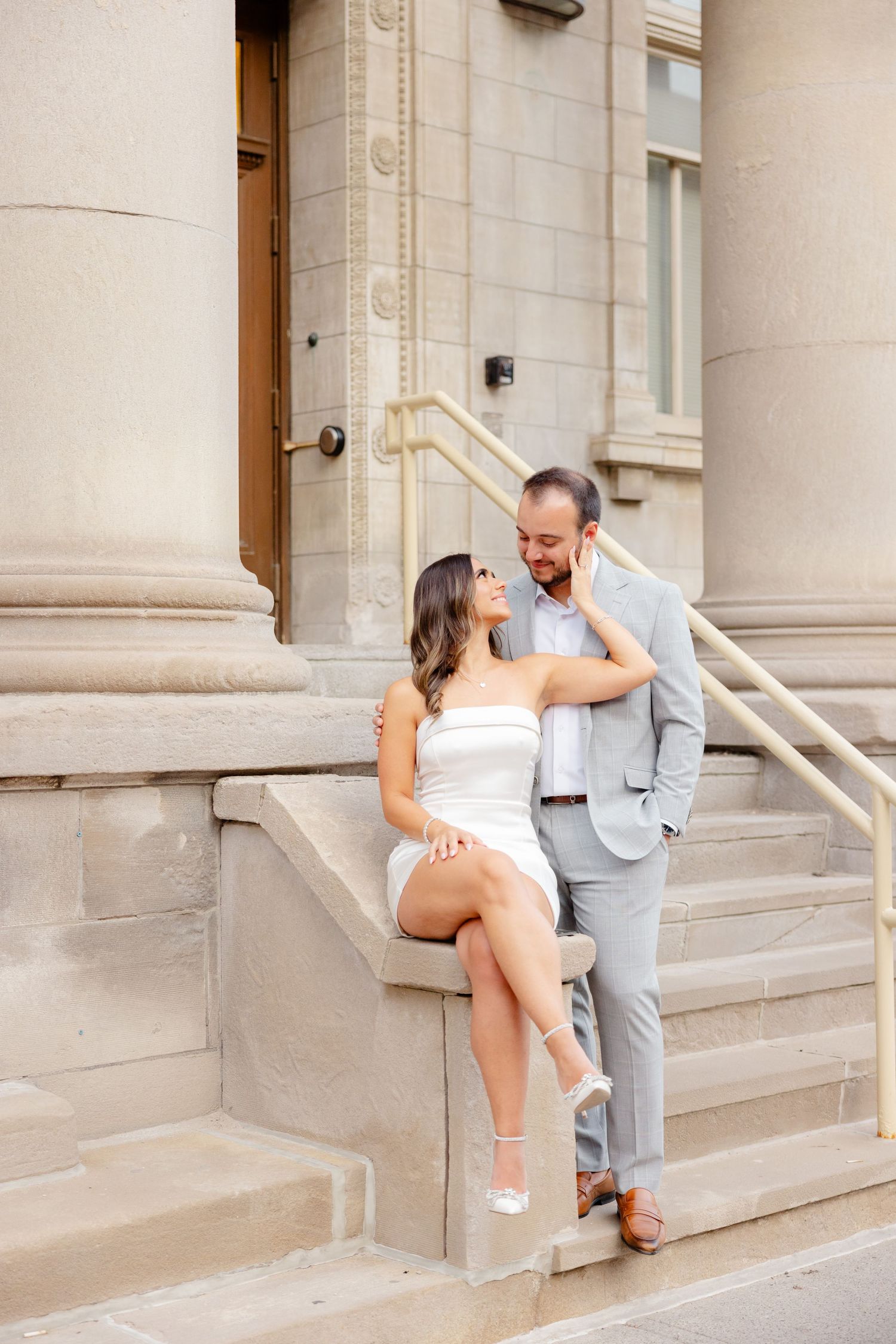 Romantic pose on classical building steps with white dress and light grey suit.