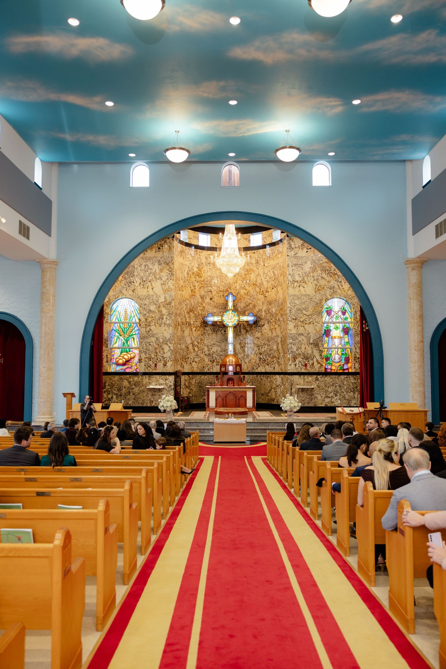 Interior of a church sanctuary with blue ceiling, red carpet aisle, and golden altar area.