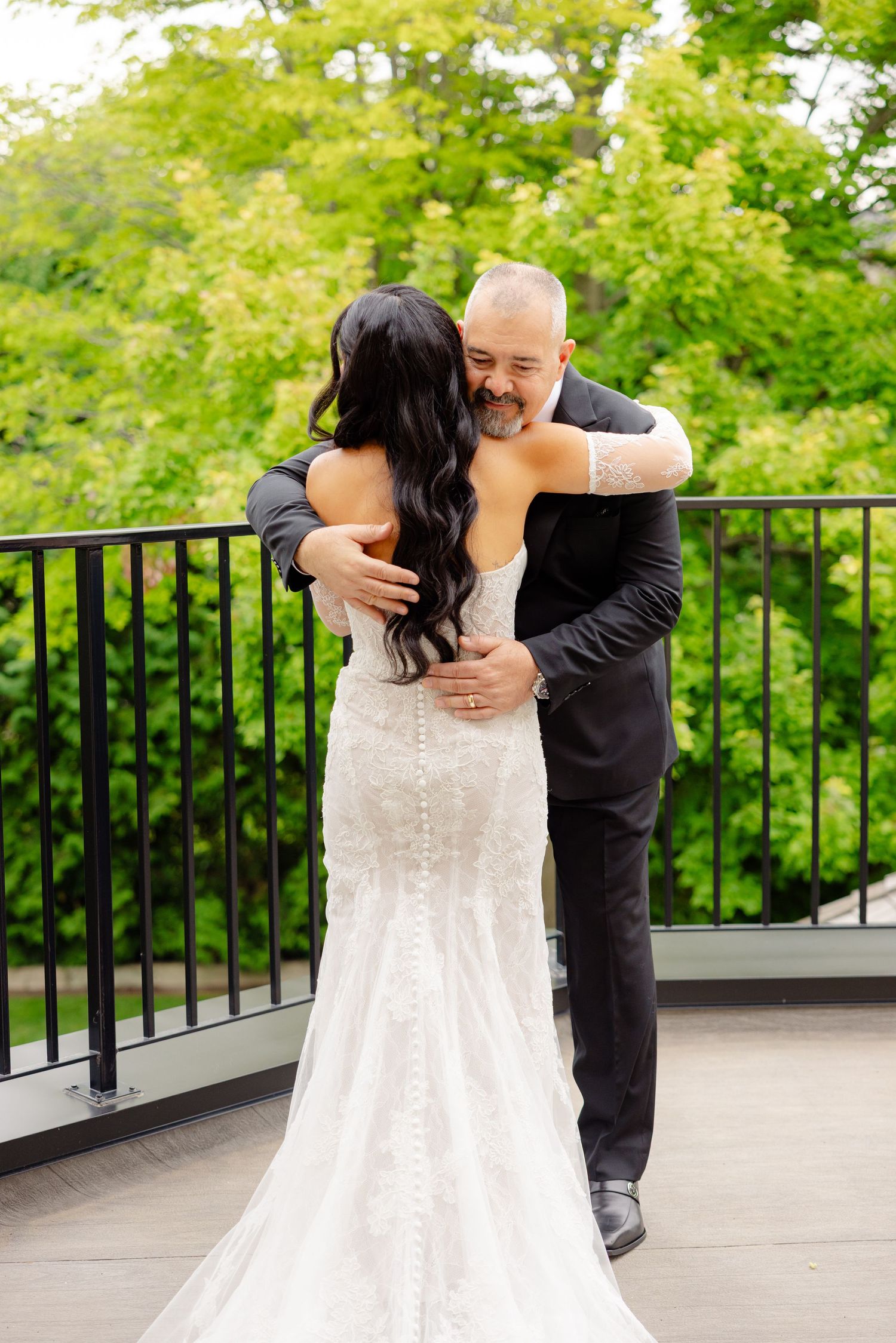 A tender moment shared between a couple during a first look wedding reveal on an outdoor deck surrounded by greenery.