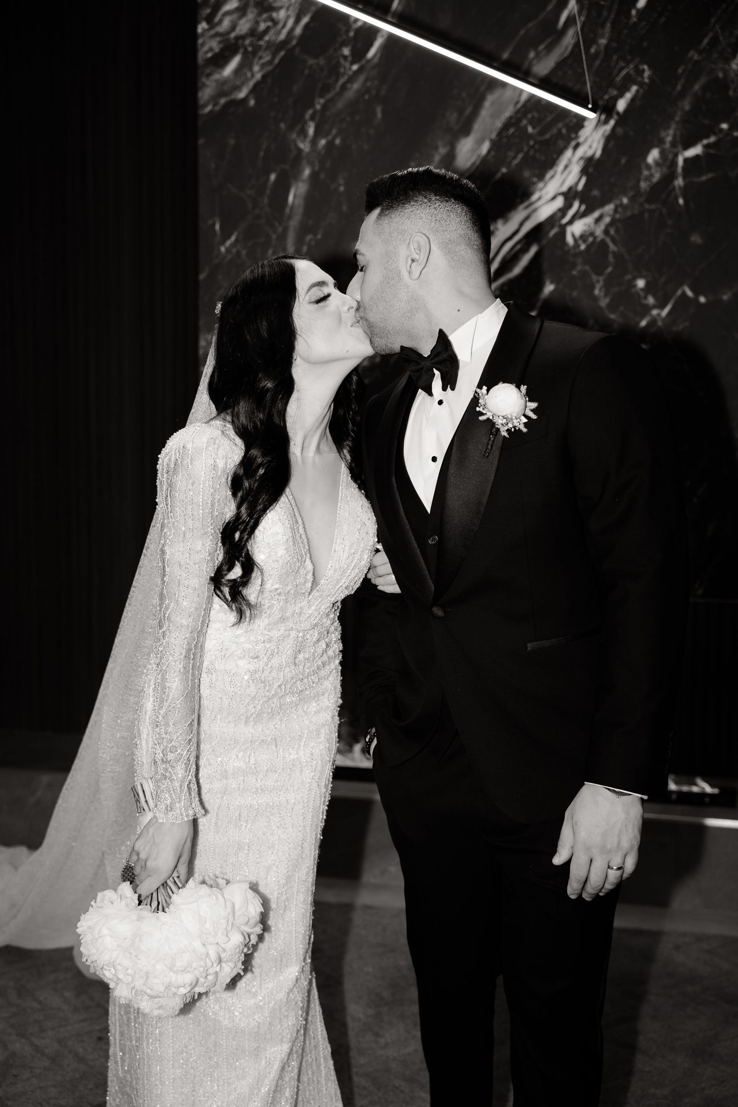 Black and white romantic wedding portrait against dramatic marble wall background.