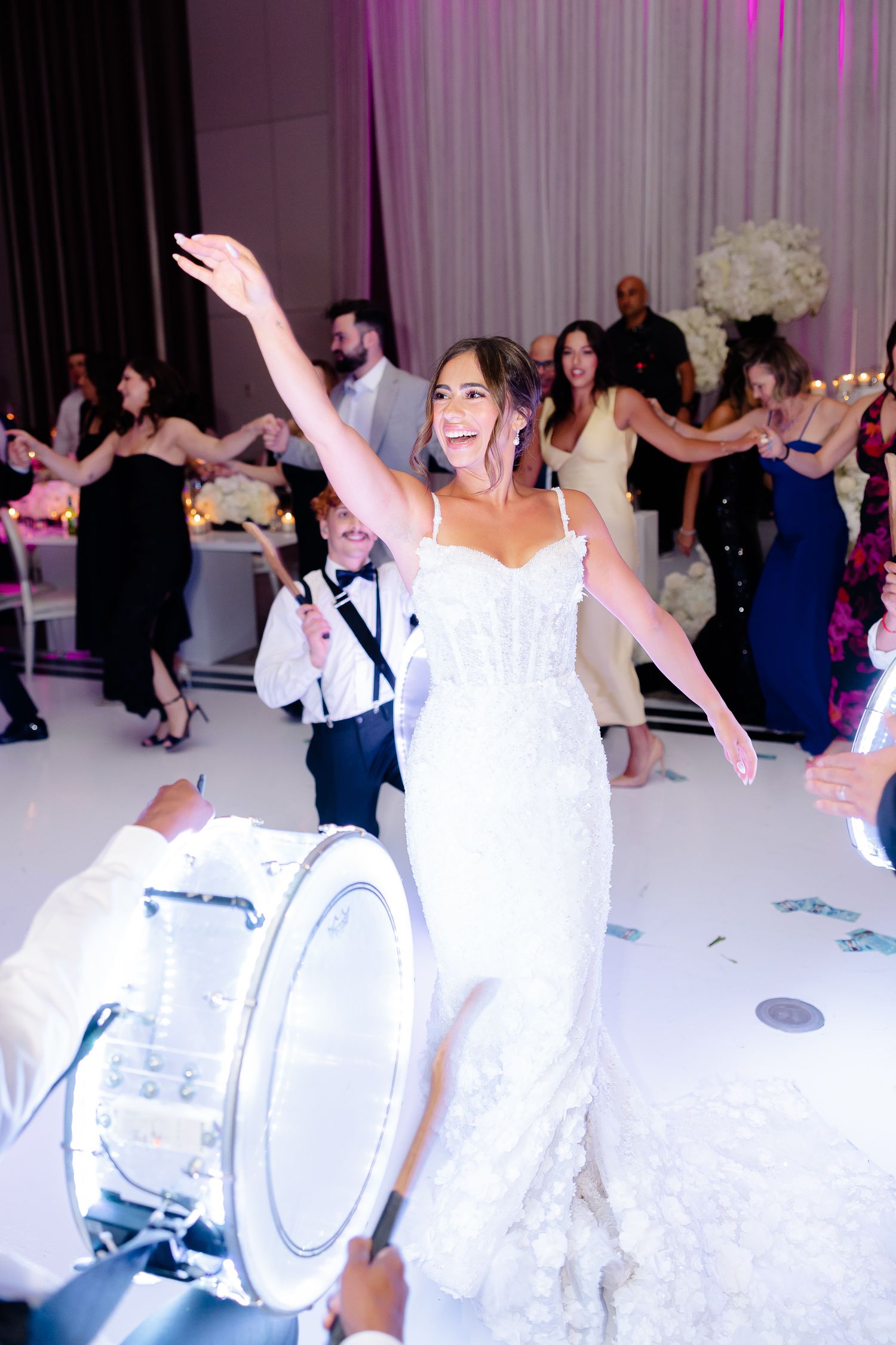 Wedding guests dance and celebrate on a white dance floor illuminated by purple lighting at an elegant reception.