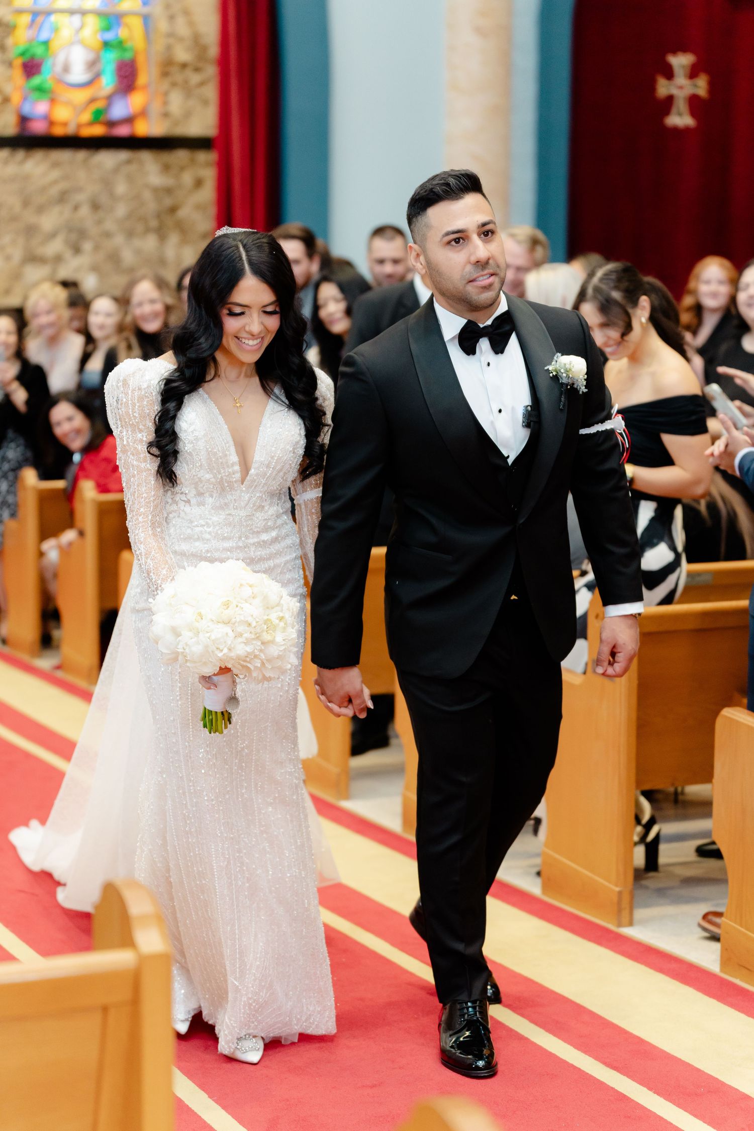 Newlyweds exit their church ceremony hand in hand on a red carpet aisle.