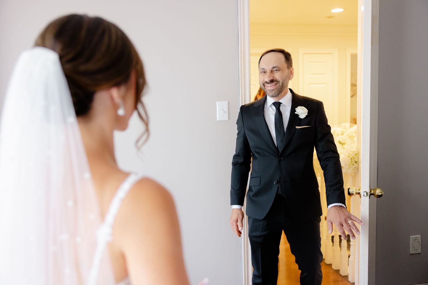 Wedding party members share emotional first look reactions in an elegant bright hallway.