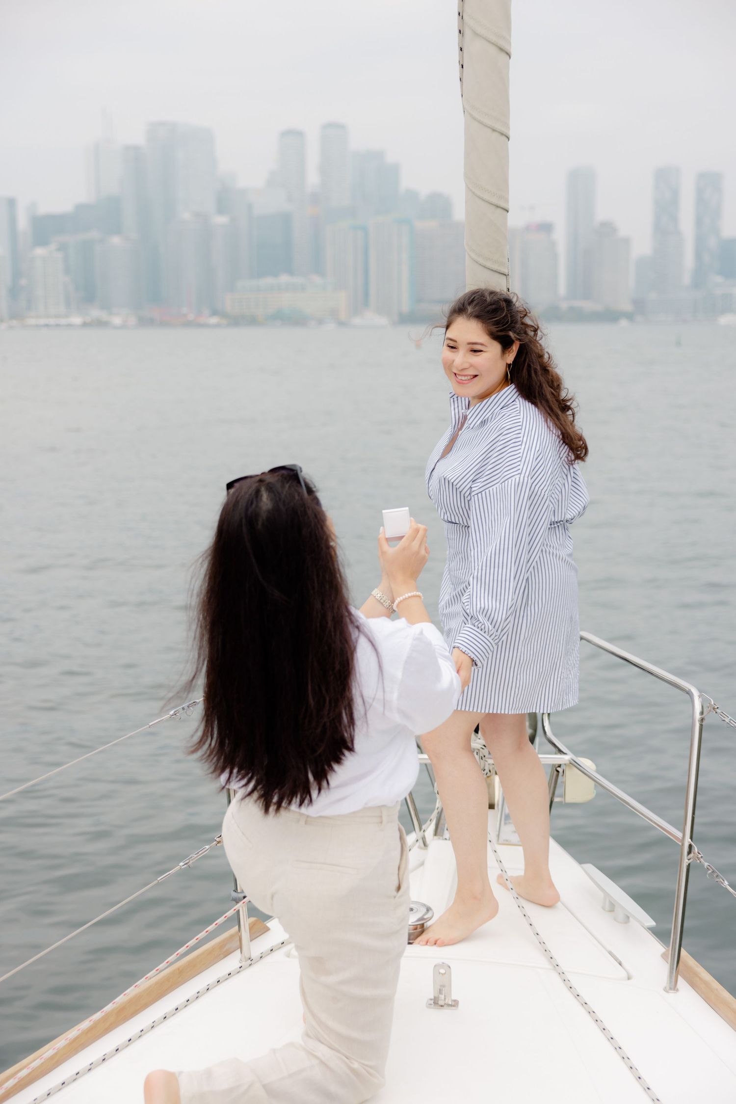 Two people enjoying a boat ride with the Manhattan skyline visible in the misty background across the harbor.
