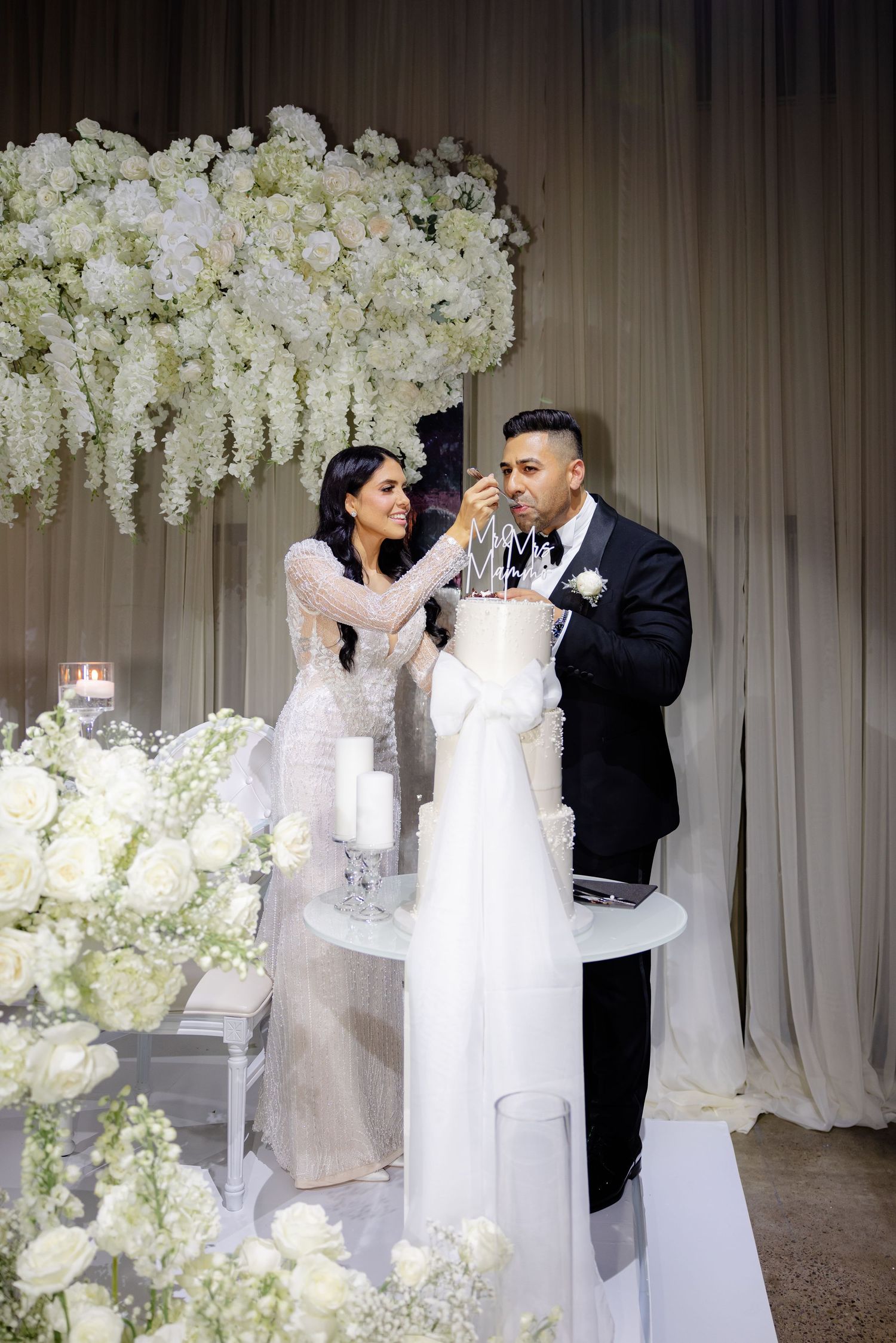 Newlyweds playfully feed each other wedding cake at their elegant reception.