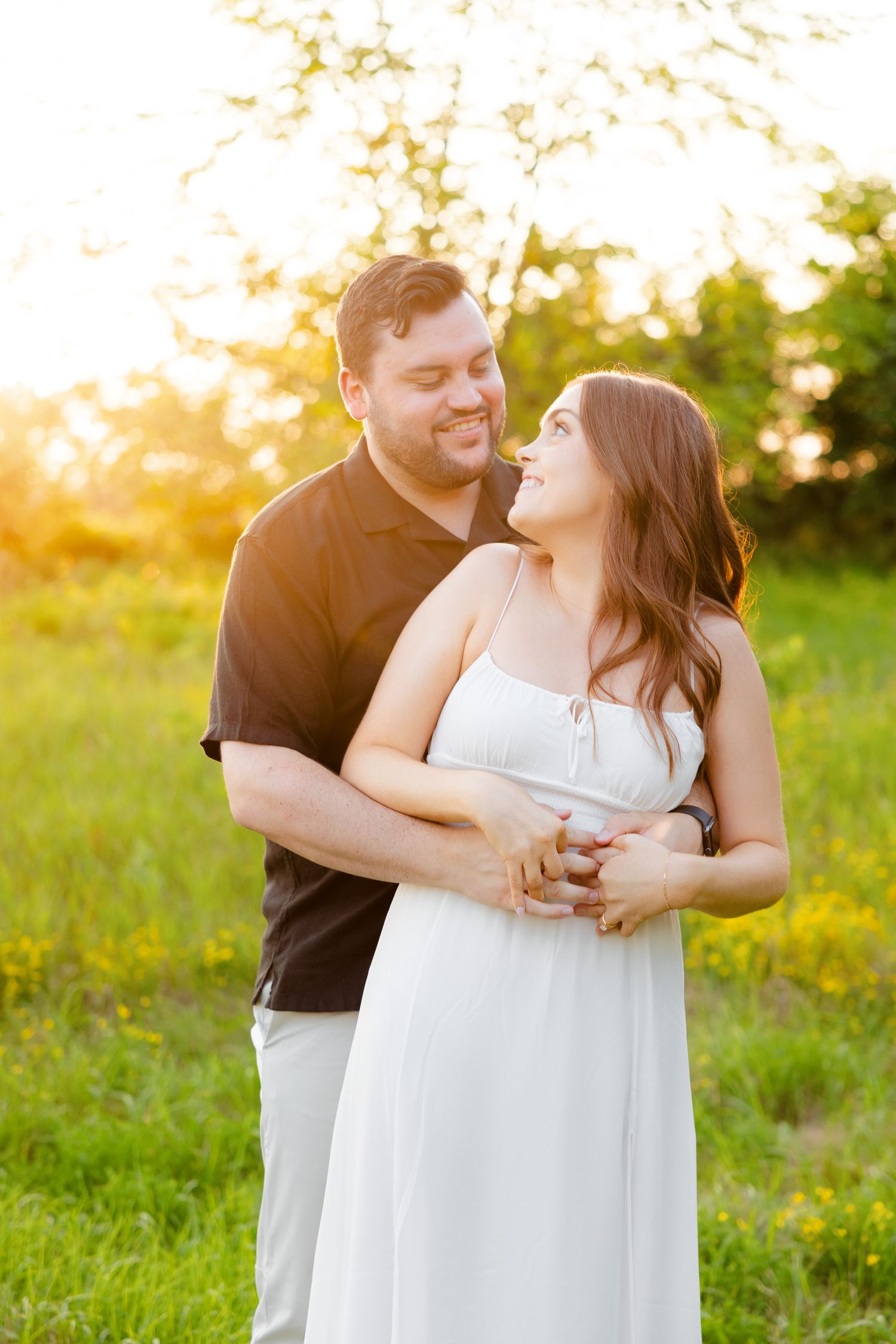 Couple embraces in a sun-drenched meadow during golden hour photoshoot, sharing a tender moment together.